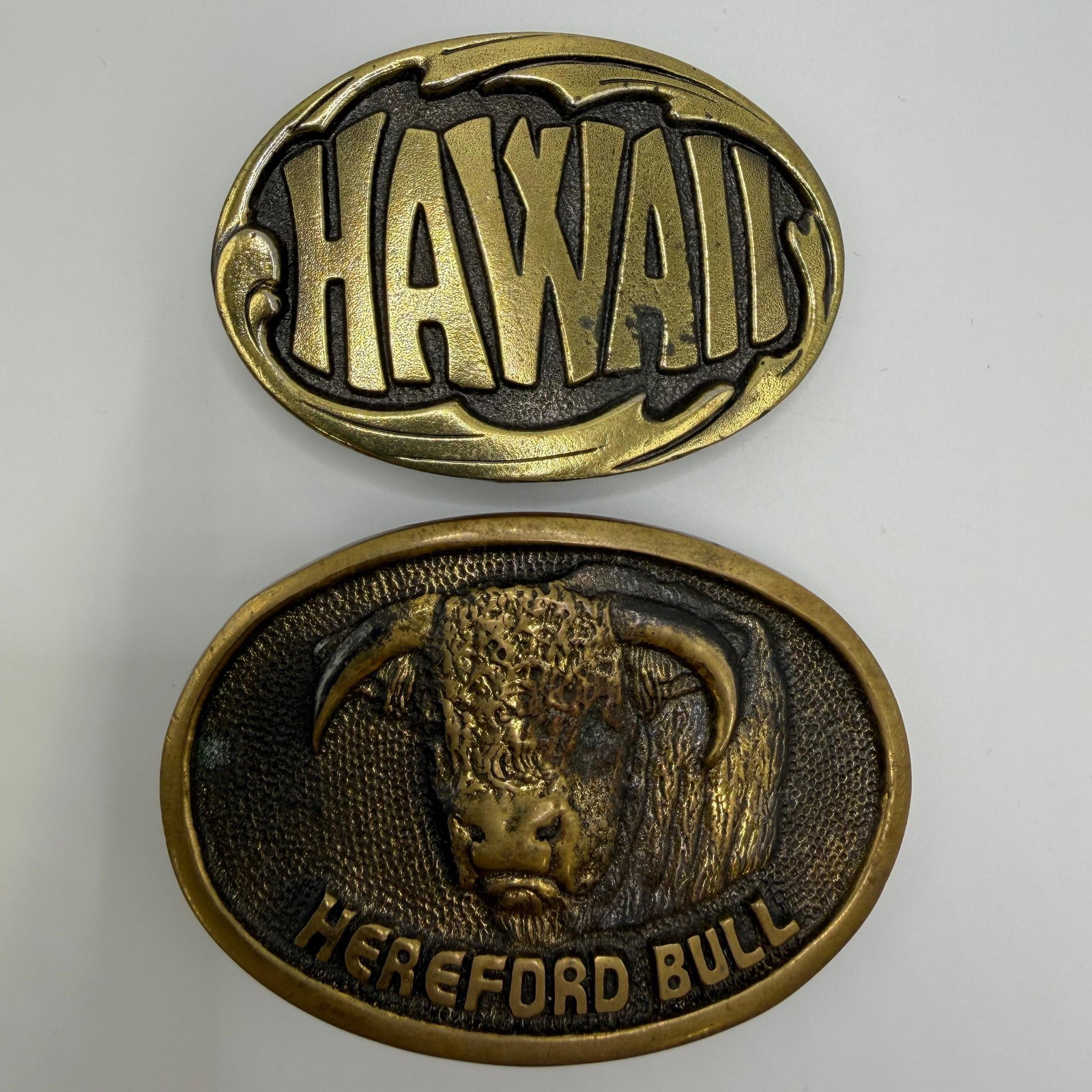 Vintage Brass Belt Buckle Hawaii and Hereford Bull by Bergamot Brass Works: Two vintage brass-tone belt buckles. Includes a "Hawaii" souvenir buckle with raised lettering and a Hereford Bull buckle by Bergamot Brass Works, dated 1978. The Hereford buckle features a de