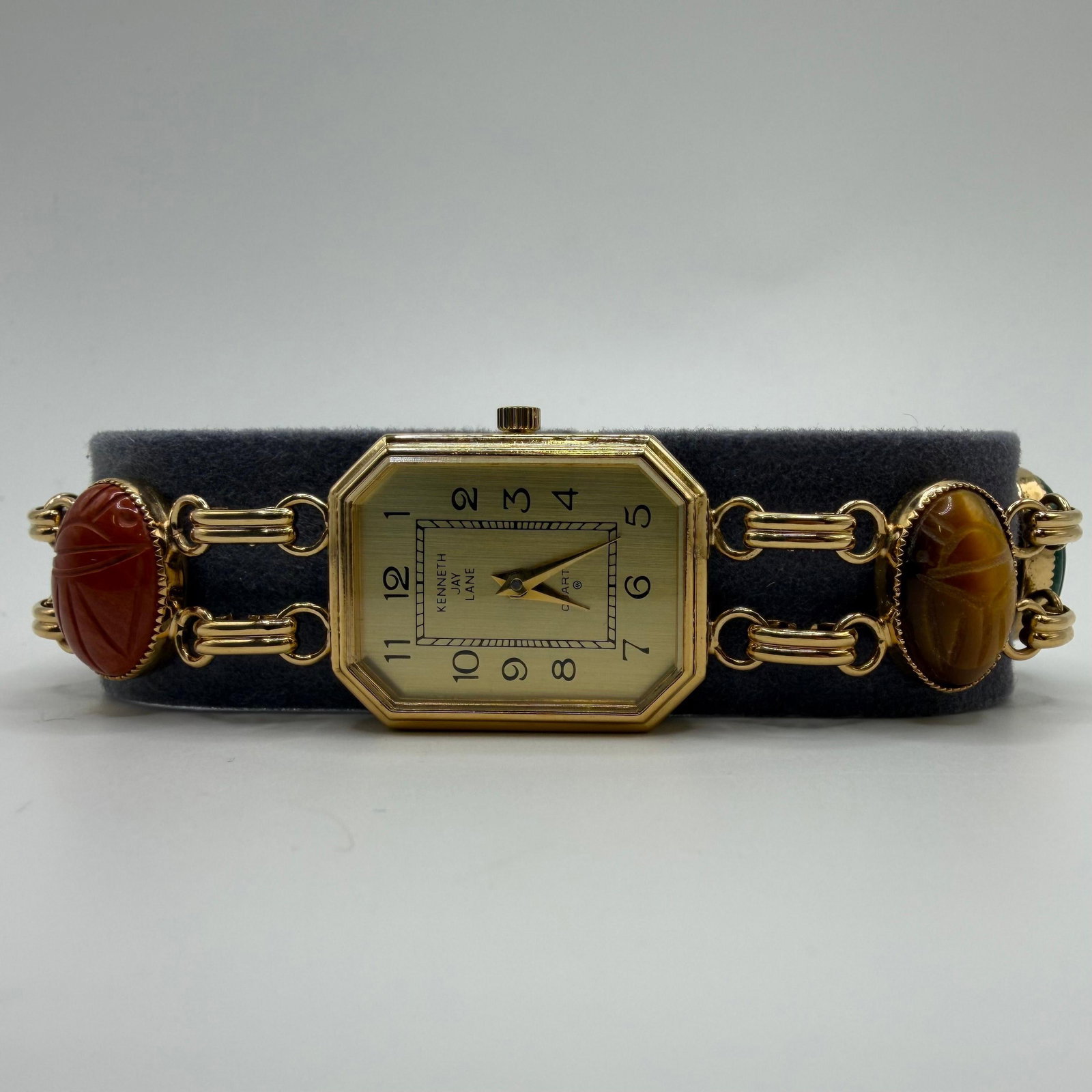 Kenneth Jay Lane Quartz Analog Gold Tone Bracelet Watch Scarab Multicolor Gemstone Link: Kenneth Jay Lane quartz wristwatch featuring an octagonal gold-tone case with a decorative link bracelet accented by carved scarab-style gemstone cabochons in assorted colors. The bracelet includes ca