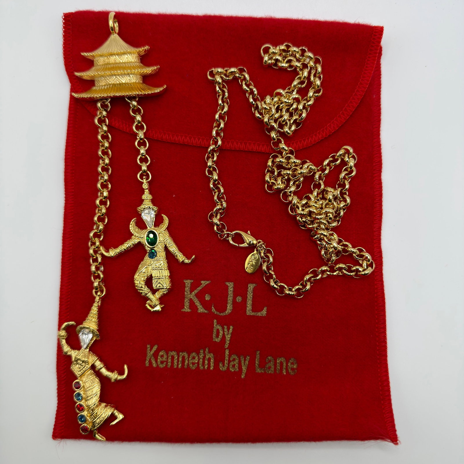 KJL Kenneth Jay Lane Figural Dancer Pagoda Pendant Necklace: KJL by Kenneth Jay Lane gold-tone figural pendant necklace featuring a Thai or Asian-inspired pagoda suspending two articulated dancer figures accented with clear, green, blue, and red rhinestones. An
