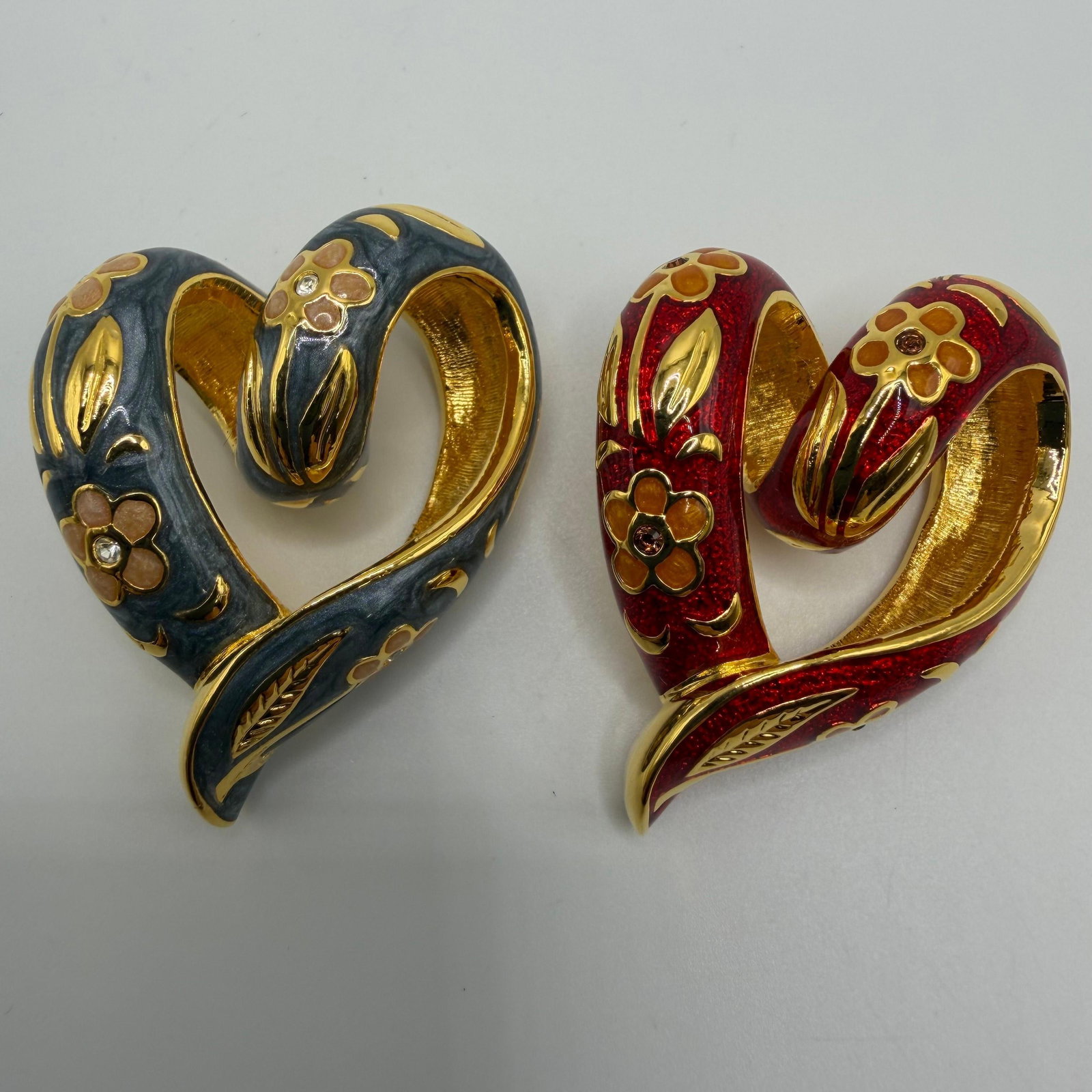 Nolan Miller Floral Enamel Cloissone Red and Gray Heart Gold Tone Necklace Pendant Set: These are Nolan Miller heart pendants featuring gray and red cloisonne enamel with gold-tone floral details and rhinestones. Includes Nolan Miller gray jewelry pouches. This item is in good pre-o