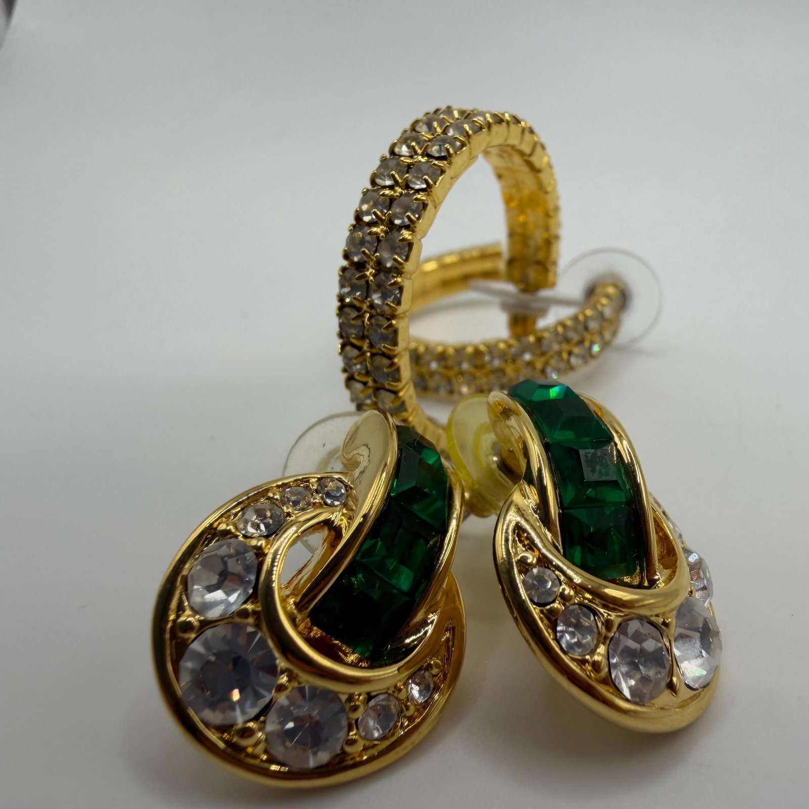 Nolan Miller Crystal Rhinestone Accent Costume Earrings HG28 Two Pairs: Collection of two pairs of signed Nolan Miller designer costume earrings. Includes a pair of gold-tone hoop earrings accented with clear rhinestones and a pair of gold-tone drop earrings featuring eme