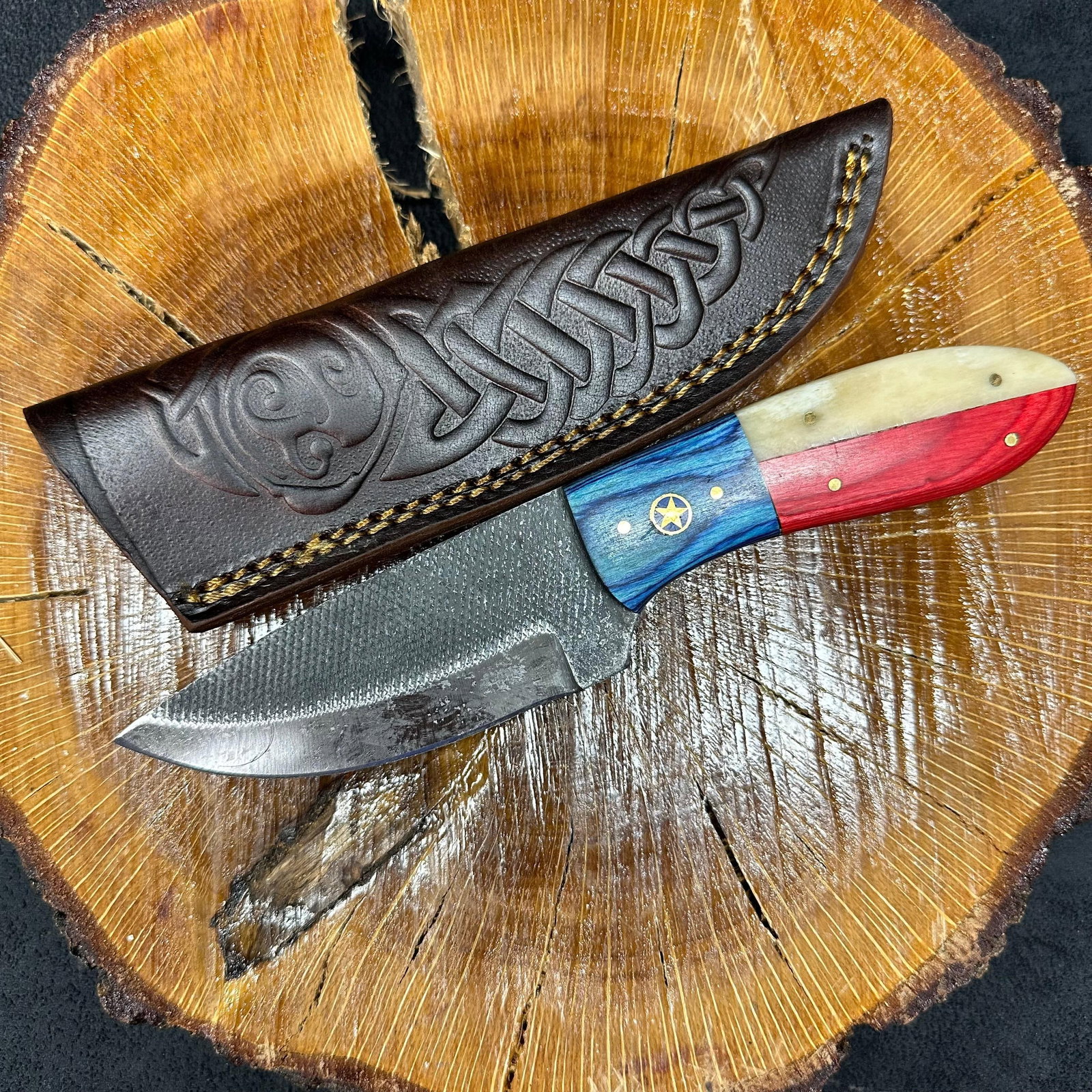 MHS Cutlery Blade Knife Red White and Blue American Themed Star Handle Q2: Fixed blade knife by MHS Cutlery featuring a textured steel blade and decorative spine work. The handle has a contoured, red, white, and blue American-themed wood/epoxy resin-style grip with metal mos
