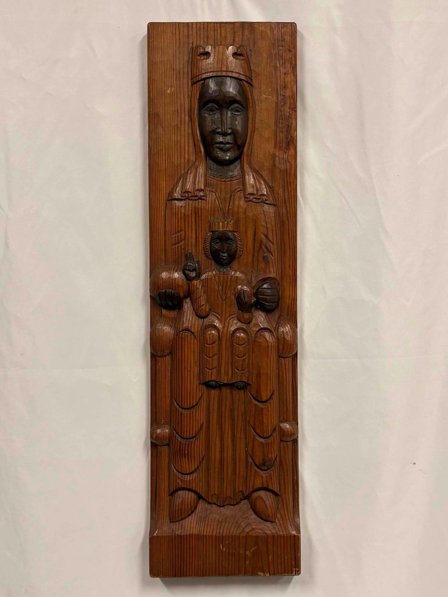 Romanesque Revival Hanging Wooden Sculpture of Madonna and Child: This item is a wooden carving is depicting the Virgin Mary and the Christ child, likely representing the "Sedes Sapientiae" or "Throne of Wisdom" iconography. The style features s