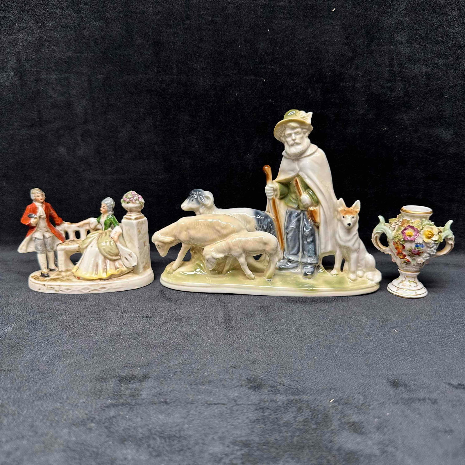 Vintage Porcelain Figurines and Decorative Vase Set of Three Decor Figures: Three vintage porcelain piece two being figures and one being a floral vase. A charming set of vintage porcelain figurines featuring pastoral scenes with shepherds, sheep, and elegantly dressed
