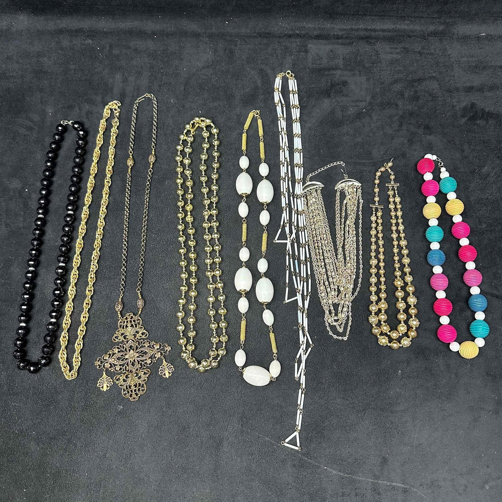 Vintage Costume Jewelry Necklace Lot Gold Tone Beaded Multicolor Statement and Mod Styles Set: Collection includes black beaded strand, gold tone rope chain, ornate filigree cross pendant necklace, gold tone bead strand, white bead and gold spacer necklace, geometric white tube bead necklace, l
