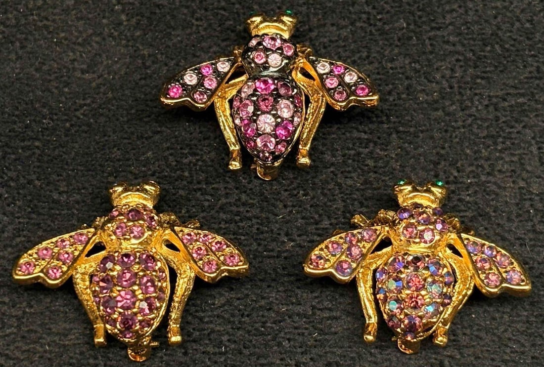 3pc Joan Rivers Rhinestone Bee Brooch Group Pink Purple Gold Tone: Group of three Joan Rivers bee brooches featuring purple and pink rhinestones, including one aurora borealis style example. Gold-tone finish with green stone eyes. Marked Joan Rivers. These costume