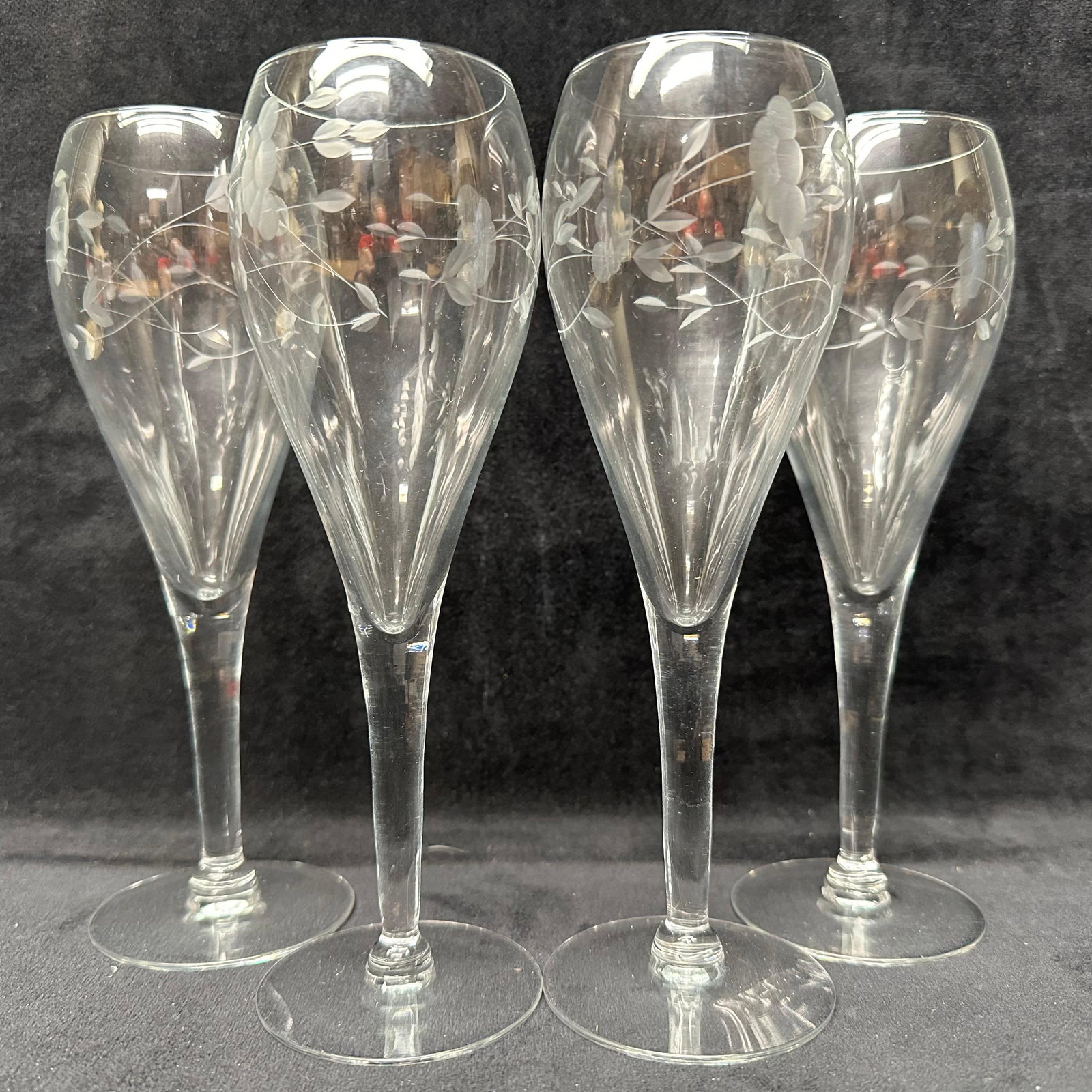 Set of Four Etched Glass Champagne Flutes Glasses: Matching group of etched glass stemware, including four champagne flutes. Each piece features hand-etched floral and vine decoration on clear glass. Slender flutes with long stems. Unmarked. These