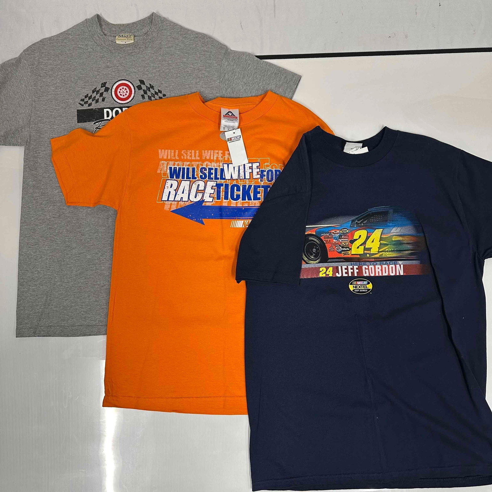 NASCAR Racing T-Shirts Dodge Jeff Gordon Novelty Race Tickets Shirt Set: Three vintage NASCAR racing t-shirts. Includes a grey Dodge Racing shirt with Dodge Motorsports and NASCAR logo, a navy Jeff Gordon #24 shirt with bold car graphic and original tags, and an orange