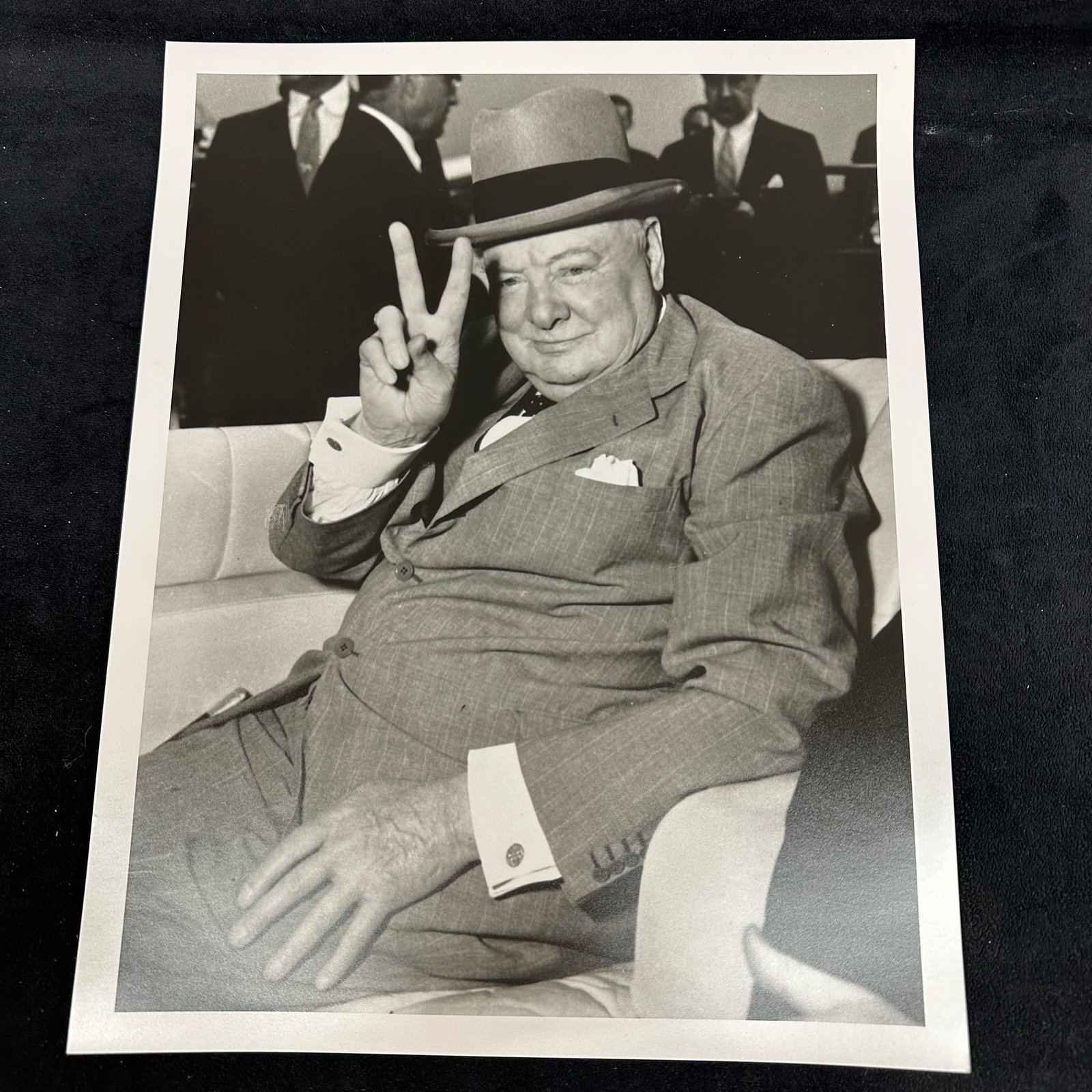 Analog Photo Print of Winston Churchill V for Victory Pose Black and White: An analog black-and-white photo print depicting Winston Churchill giving his iconic “V for Victory” hand gesture. Churchill is shown seated in a suit and hat, exuding his characteristic de