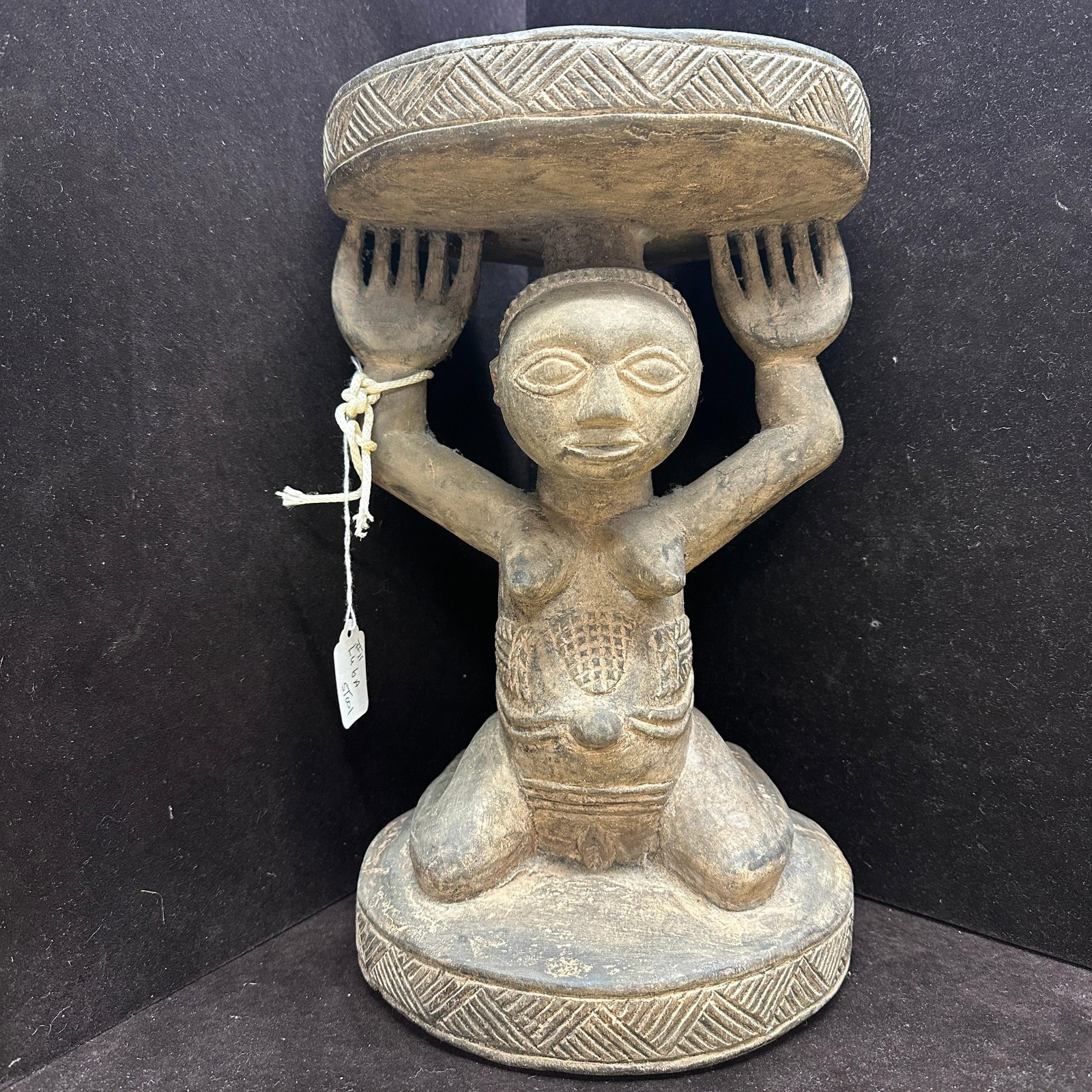 Luba Caryatid Stool Carved Wood Female Figure Mukuni Village Zambia: Carved wood stool in the form of a kneeling female caryatid figure, attributed to the Luba peoples. The figure supports a circular seat with a geometric carved border. Features include stylized facial