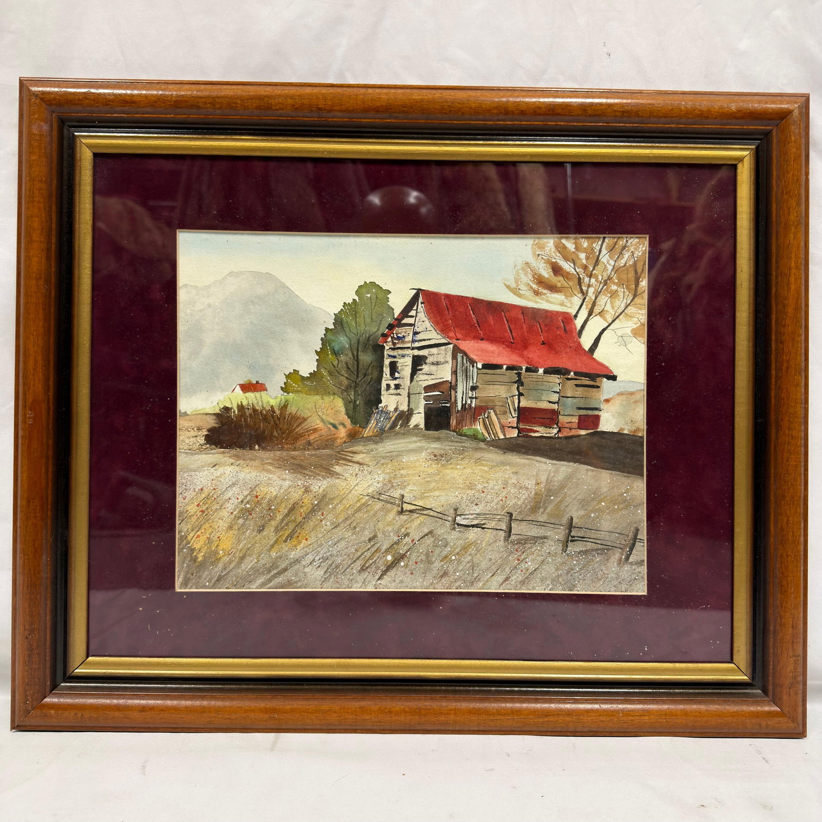 The Red Roof Shed Original Watercolor Painting Framed Artwork: Original watercolor depicting a rustic rural shed with a prominent red roof, mountain landscape, trees, and split-rail fence. Verso retains a gallery/artist label identifying Marie Williams Watercolor