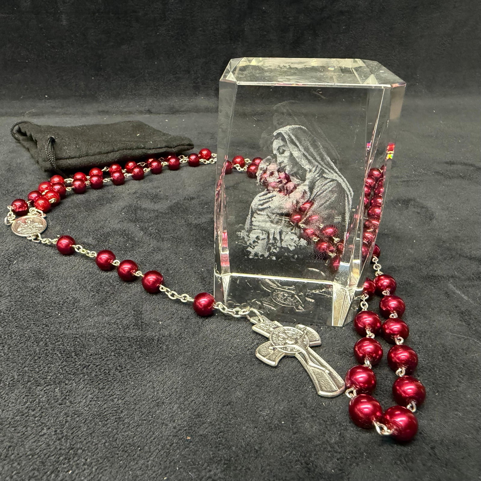 Religious Rosary and Madonna Glass Crystal Display: Religious devotional lot featuring a red/maroon beaded rosary with crucifix and St. Agatha prayer medal, accompanied by a clear crystal block depicting the Madonna and Child. Includes a black storage 
