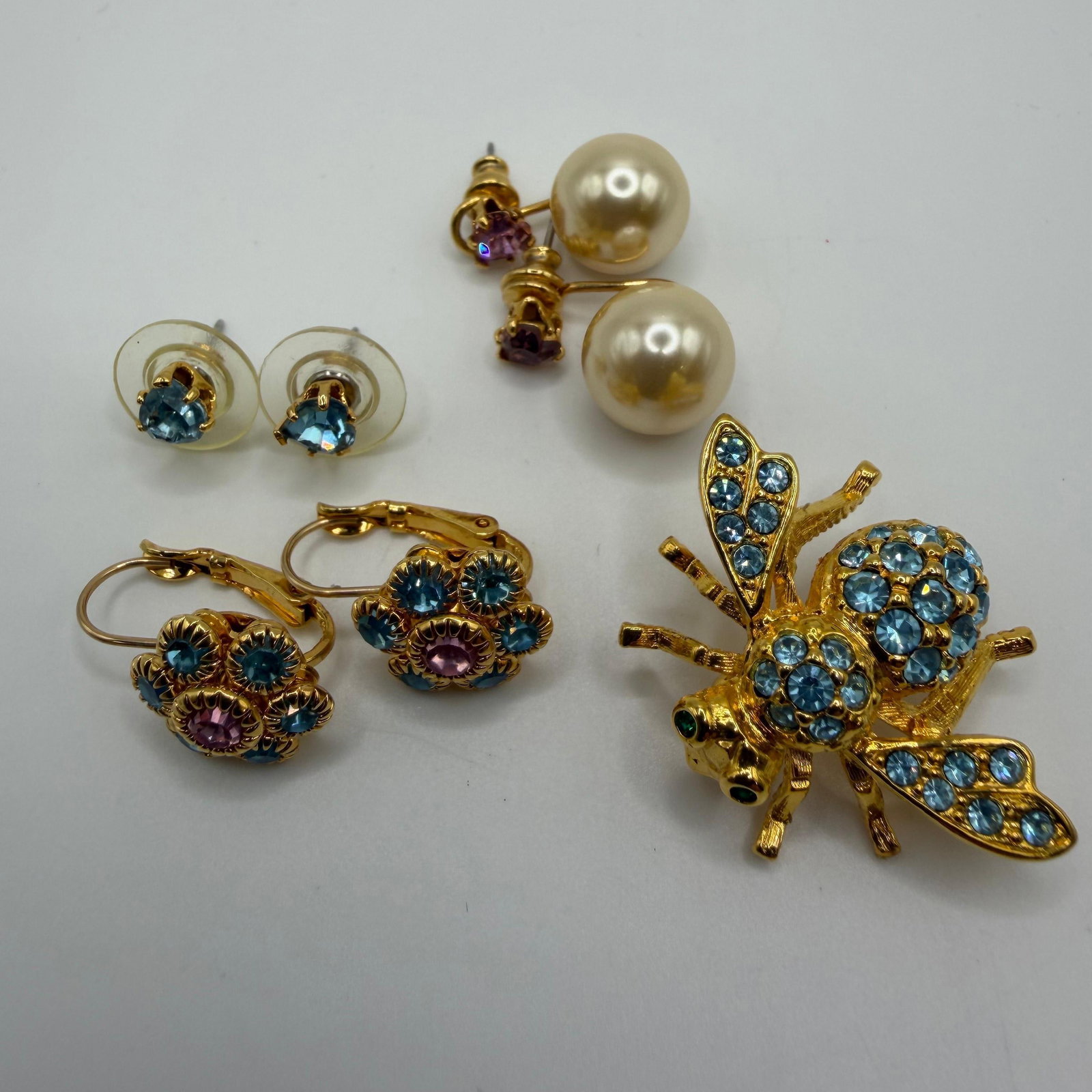 Joan Rivers Blue Purple Crystal Bee Brooch and Flower Earrings HH27: Joan Rivers jewelry lot featuring a blue crystal bee brooch with green crystal eyes, a pair of blue crystal stud earrings, floral blue and lavender purple crystal lever back earrings, and a pair of fa