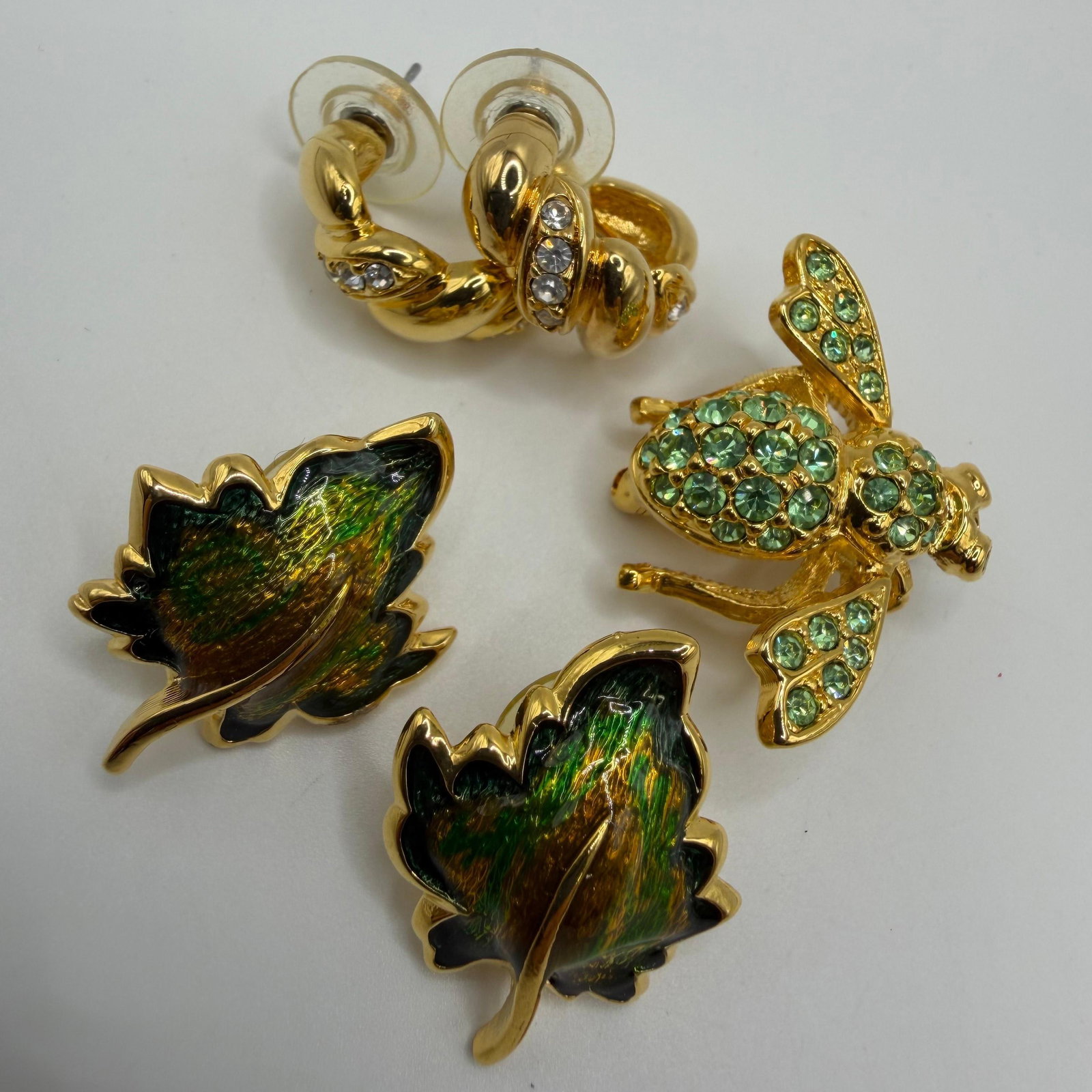Joan Rivers Green Enamel and Rhinestone Jewelry Set HH35: A lot of Joan Rivers costume jewelry, including a green rhinestone bee brooch, a pair of iridescent green/yellowish enamel leaf earrings, and a pair of gold-tone half-hoop earrings accented with clear