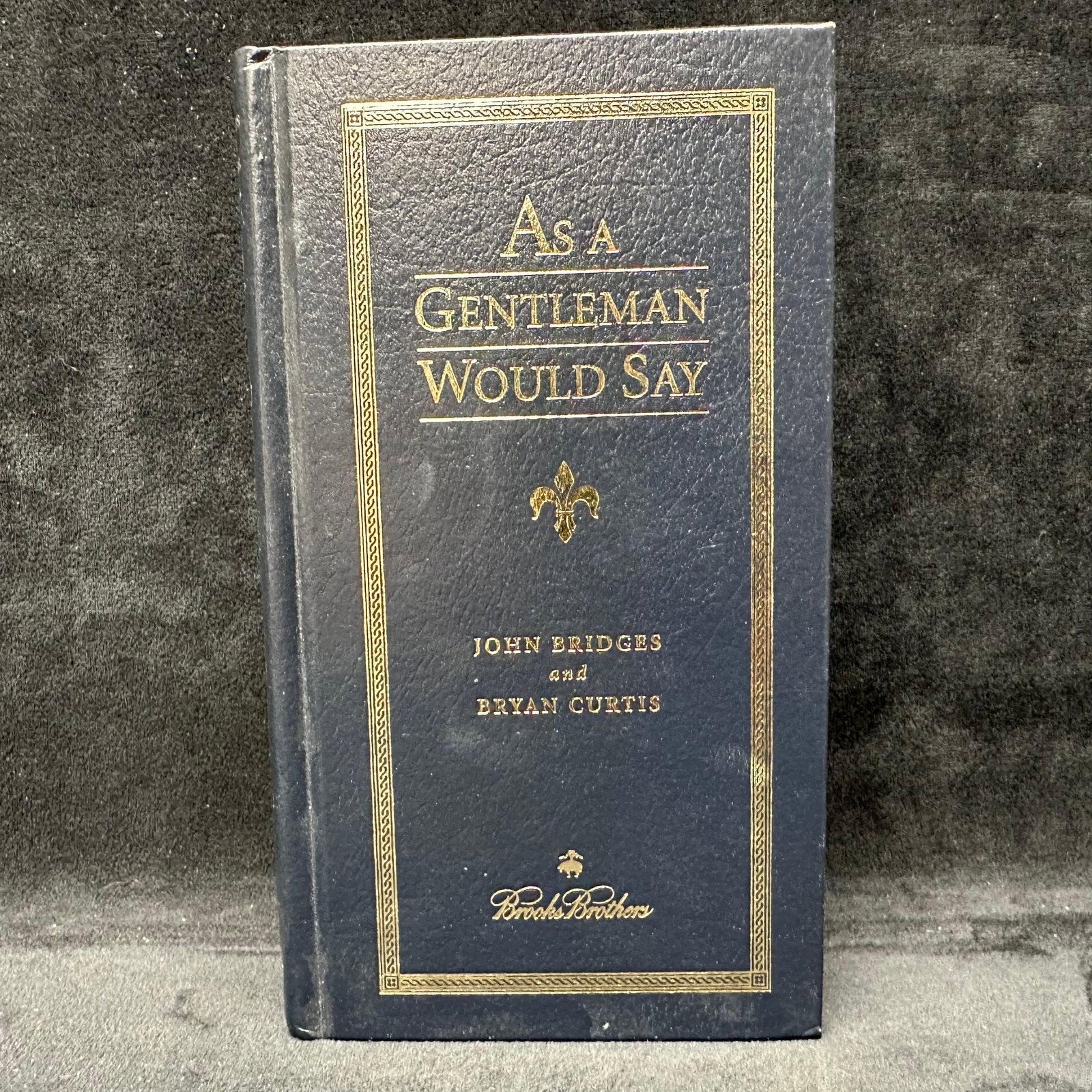 As A Gentleman Would Say Signed Hardcover Brooks Brothers Book: Signed with a personal inscription to Michel Roux. Condition shows general handling wear, scuffing, and surface marks to the cover consistent with age. Interior pages appear intact. This item is in go