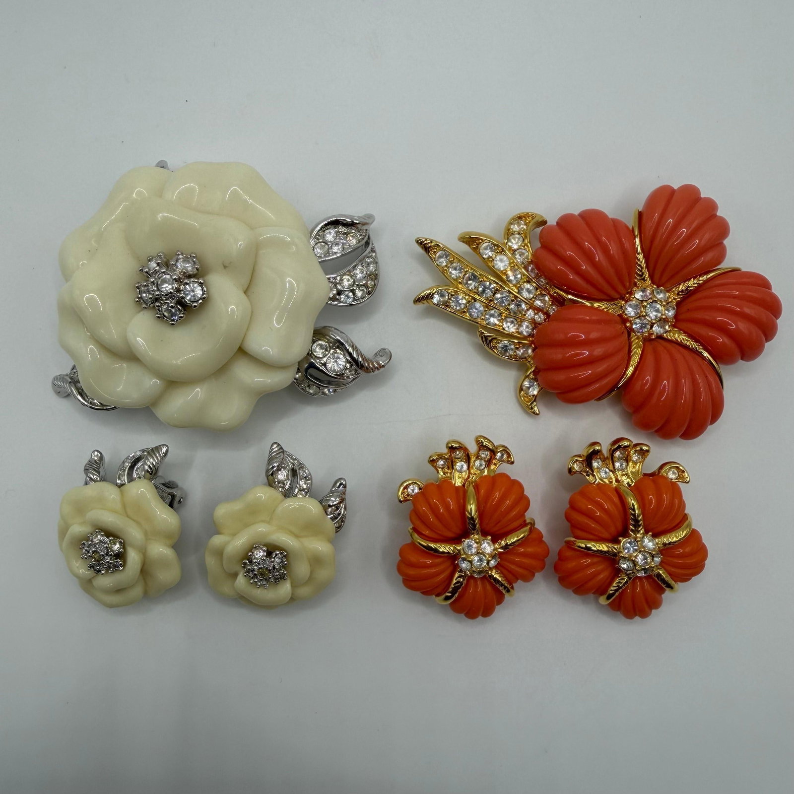 Nolan Miller Floral Costume Jewelry Brooch and Earring Sets: Two coordinated vintage costume jewelry floral sets. Includes signed Nolan Miller coral-colored flower brooch with matching clip-on earrings featuring rhinestone accents, and a signed ivory-tone molde