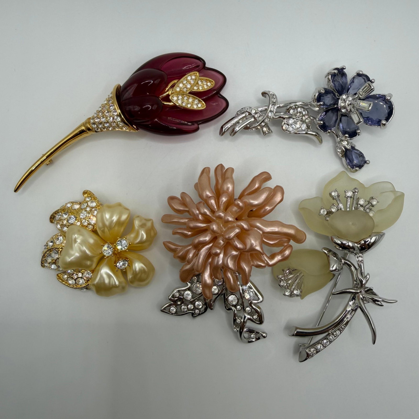Nolan Miller Designer Floral Fashion Brooches Five Flower Themed: Collection of five signed Nolan Miller designer floral brooches in gold-tone and silver-tone finishes. Includes a burgundy lucite-style tulip with crystal accents, blue crystal flower spray, cream ena