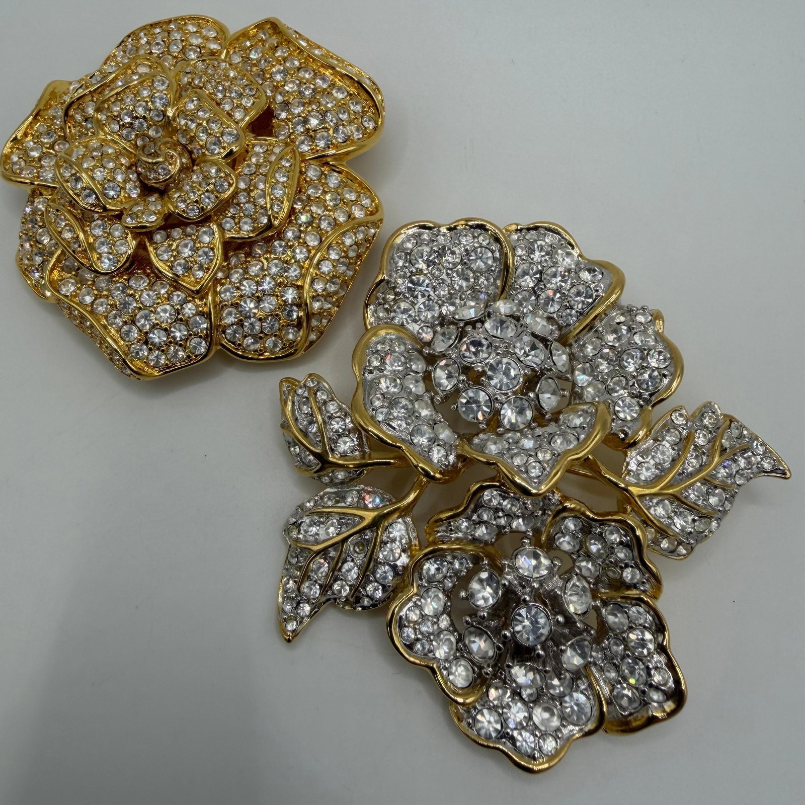 Nolan Miller Gold Tone Clear Rhinestones Leaves and Floral Designer Brooches: These brooches are marked Nolan Miller. Featuring a pave clear crystal rhinestone accents in a gold tone framing. These items are pre-owned, with light wear, minor imperfections, and surface scratches