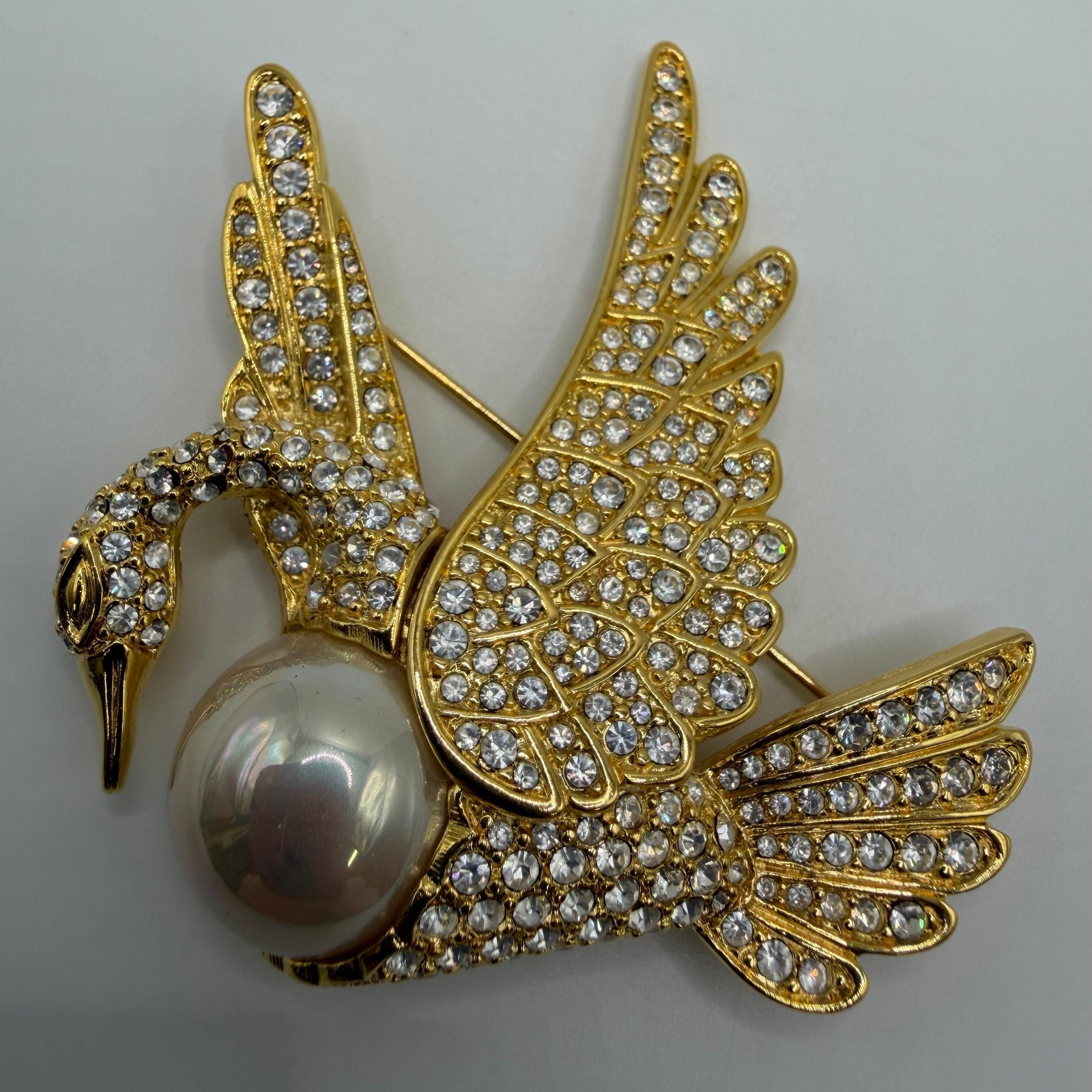 Nolan Miller Fantasy Flight Swan Brooch Large Faux Pearl Rhinestone Crystals AB30: This is a Nolan Miller designer brooch featuring a Fantasy Flight swan brooch that features a large faux pearl set against a gold-tone body filled with pave diamond-style crystals/rhinestones. Th