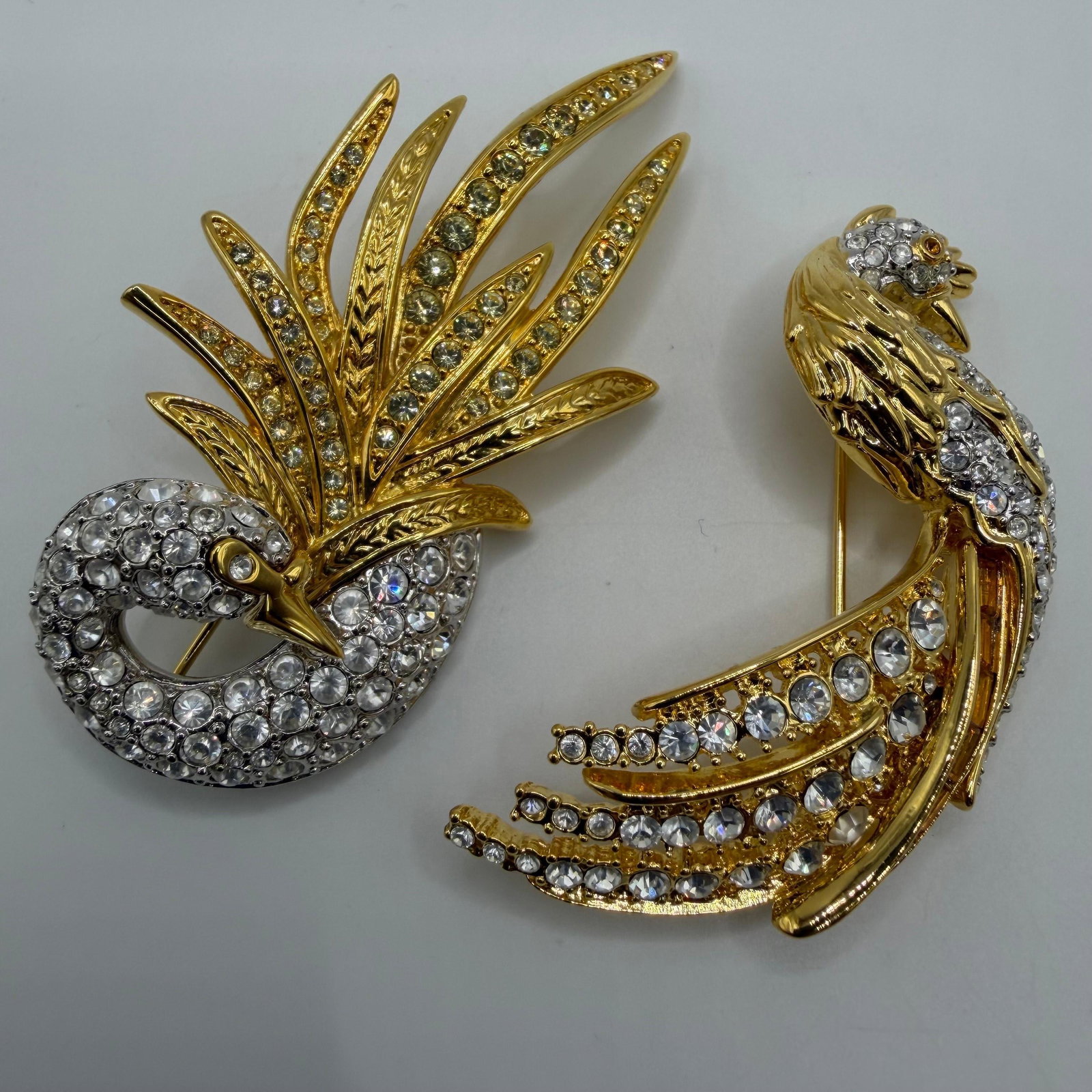 Glamour Collection Nolan Miller Rhinestone Bird Brooches AB24: Pair of signed Nolan Miller designer costume brooches, including a stylized cockatoo-type bird with clear rhinestones and a gold-tone feather crest, and a tropical parrot featuring clear rhinestones w