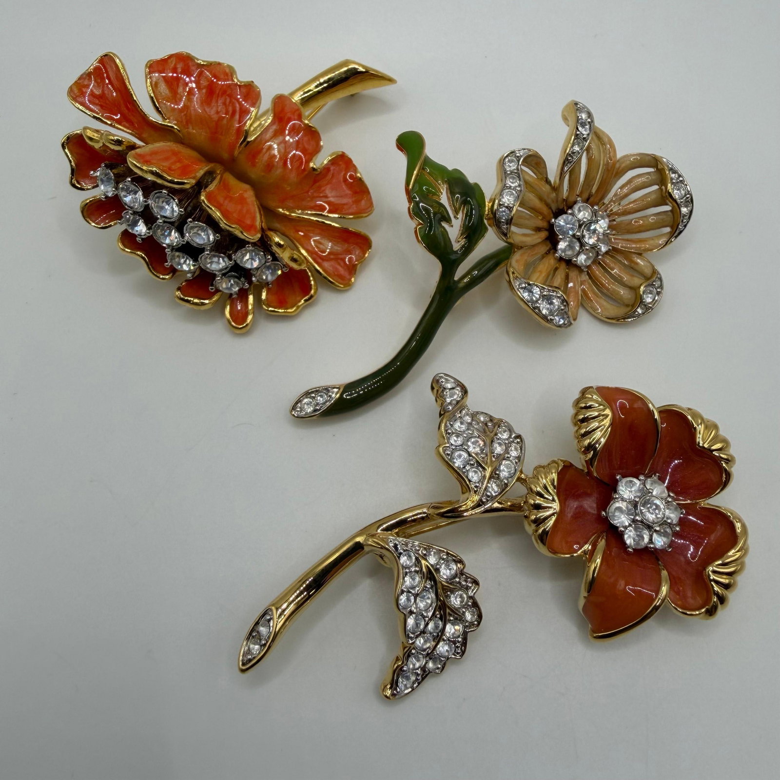 Group of Three Nolan Miller Floral Enamel and White Clear Rhinestone Designer Brooches AB22: Group of Three Nolan Miller featuring a floral or flower theme, with enamel and white clear rhinestone accents. All pieces are marked Nolan Miller on the reverse. These items are pre-owned, with light