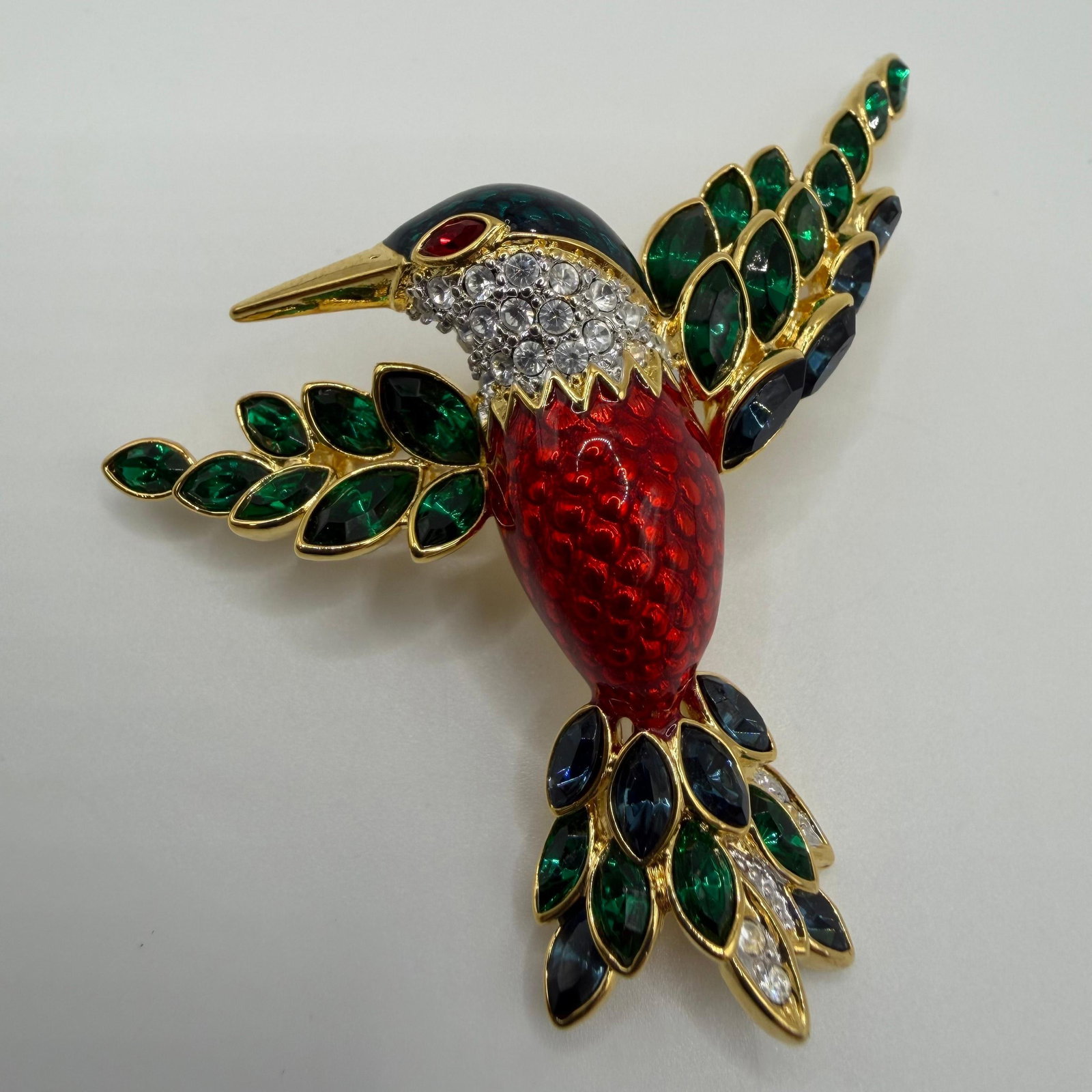 Nolan Miller Jacobin Hummingbird Glamour Collection Brooch AB29: A detailed figural hummingbird featuring crystal accents, with a textured red enamel body and green enamel wing tips. Hallmark Nolan Miller on the reverse. This item is pre-owned, with light wear, min