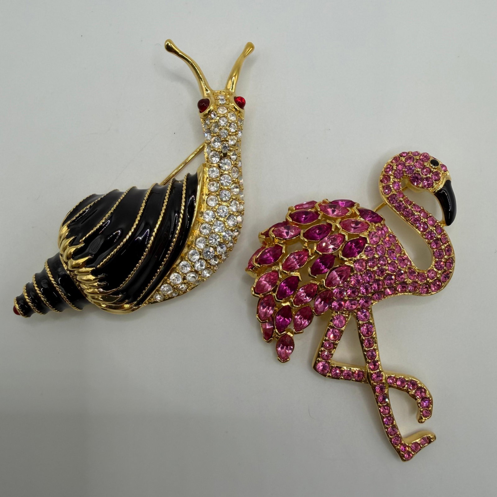 Pink Rhinestones Flamingo and Black Enamel Snail Pair of Nolan Miller Brooches AB27: Pair of Nolan Miller designer costume brooches, including a pink rhinestone flamingo and a black enamel snail accented with clear rhinestones and red crystal eyes and back-end tail. Both are signed No