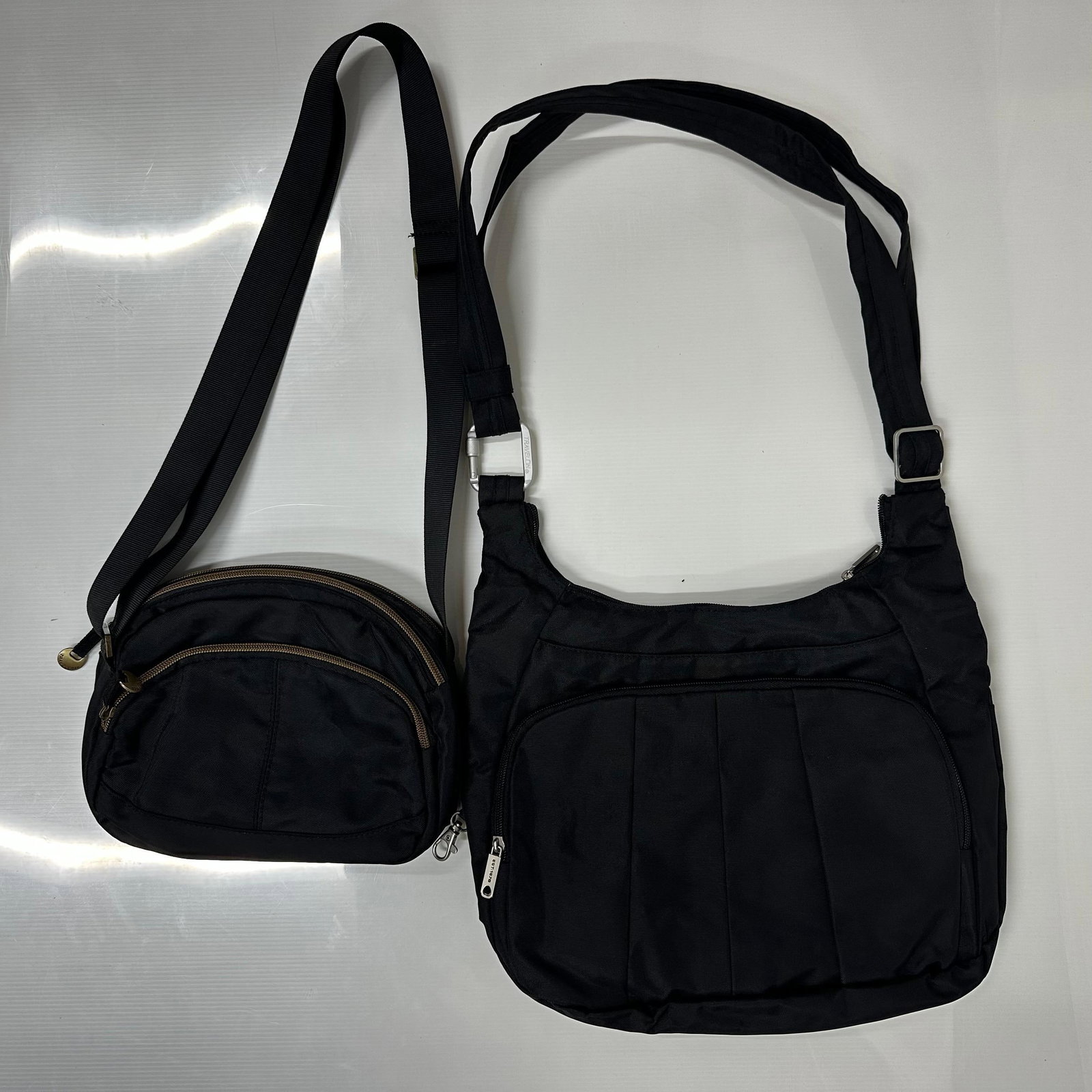 Travelon 2 Black Nylon Crossbody Handbags with Detachable Wallet Pouch: The lot includes two Travelon brand black nylon crossbody and shoulder handbags. One is a larger slouch-style shoulder/crossbody bag with an adjustable strap, multiple zippered