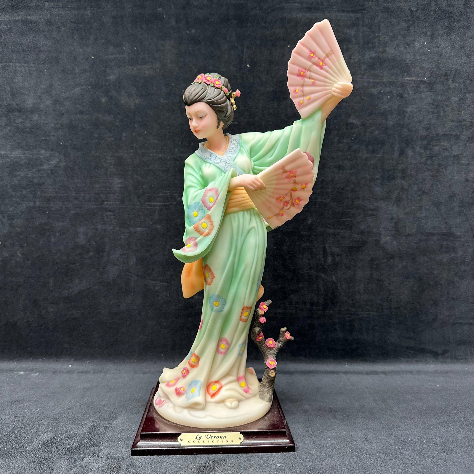La Verona Fan Dancer Figurine Girl Geisha Cherry Blossom Kimono: This vintage resin figurine depicts an oriental dancer with cherry blossom details on her kimono and fan. The broken hand has been repaired. Glue residue. This item is in pre-owned, previously