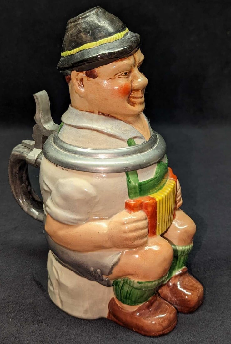 Vintage West German Man With Accordion Stein: Vintage West German Man With Accordion Stein. This lidded ceramic stein is approx 5" x 6 3/4" x 9" and it weighs 2.45 lbs. The stein is in a good, vintage condition with no chips or cracks. There are 