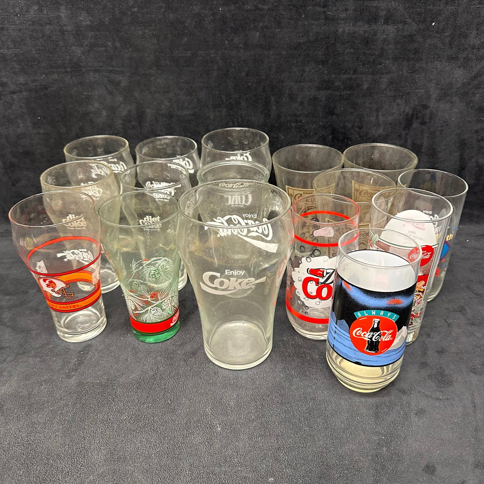 Collection of Coca Cola and Diet Coke Advertising Glassware Glass Cups: A group of assorted Coca-Cola and Diet Coke drinking glasses featuring various logo styles, promotional designs, and themed graphics. Includes mixed sizes and shapes, such as tumblers and handled