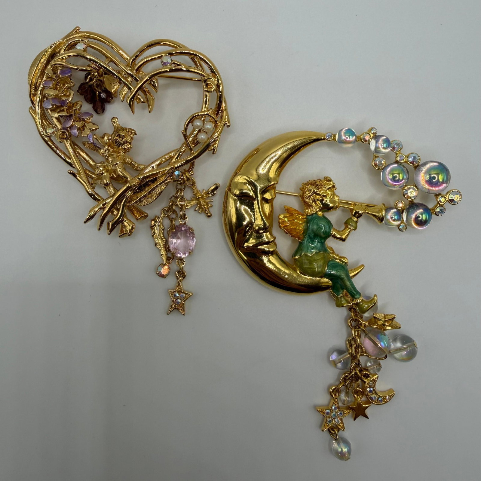 Pair of Kirks Folly Pipedream Fairy and Heart Wisteria Fantasy Brooches: Pair of whimsical Kirks Folly gold-tone fantasy brooches. Includes an openwork heart-shaped fairy brooch accented with flowers, faux pearls, faceted crystals, and dangling celestial charms, along with