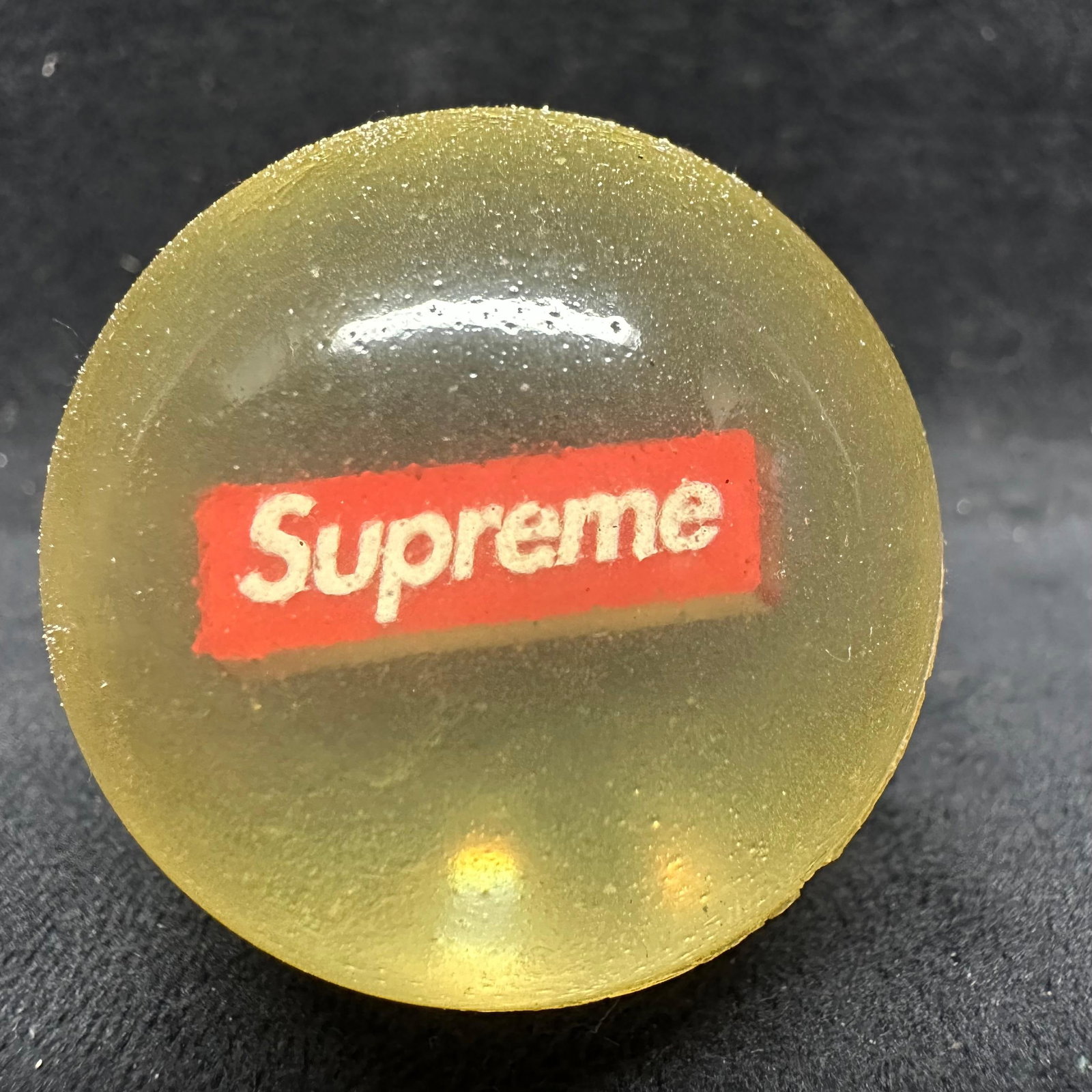 Supreme Translucent Logo Bouncy Ball with 23 Drawstring Pouch: Supreme translucent rubber bouncy ball featuring the iconic red box logo suspended inside. Includes original white drawstring pouch marked 23. The ball shows light surface wear and minor scuffs consis