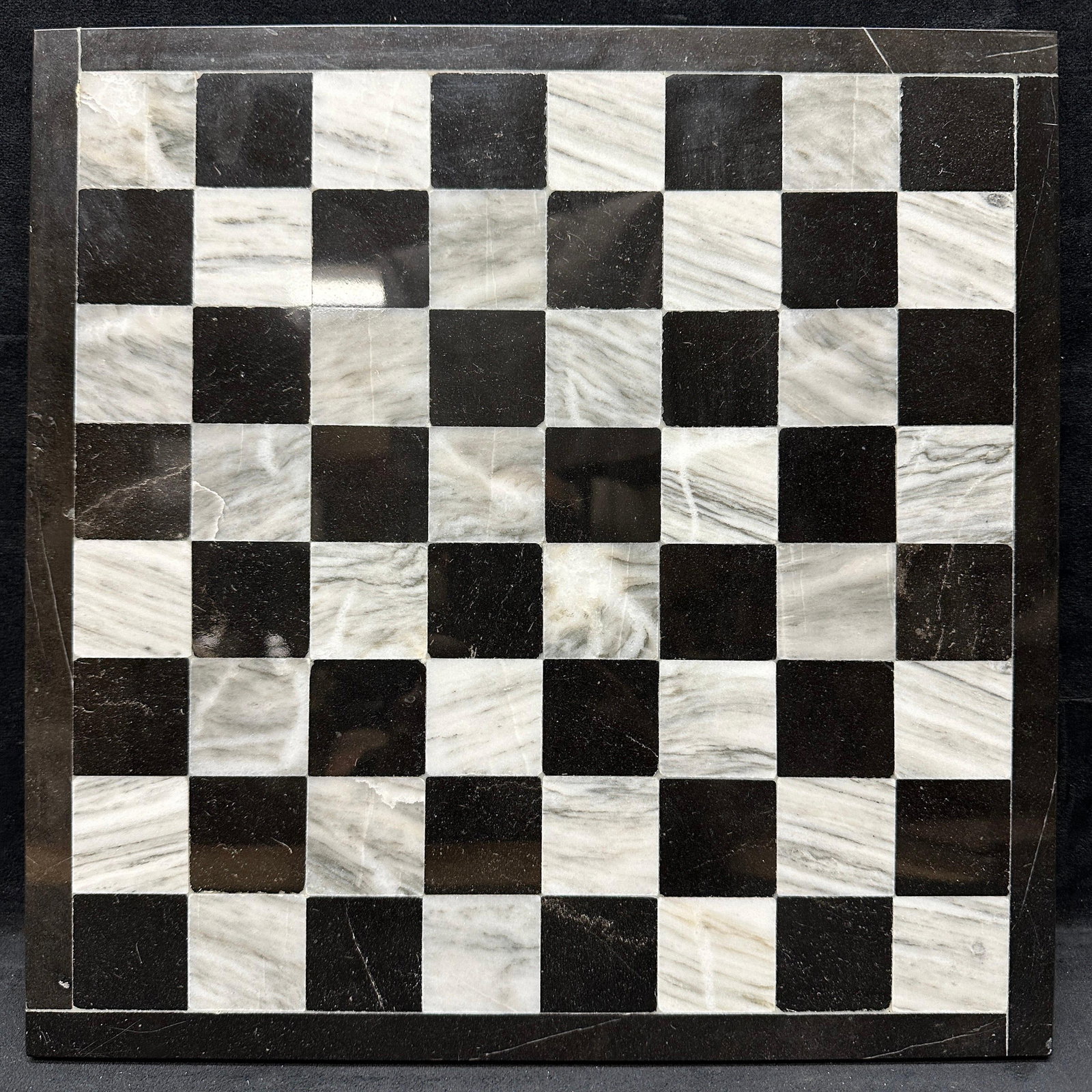 Black and White Marble Chess Board: Polished stone chessboard featuring alternating black and white marble squares with a matching dark stone border. Standard 8x8 layout. Shows surface wear, including scratches and edge wear consistent 