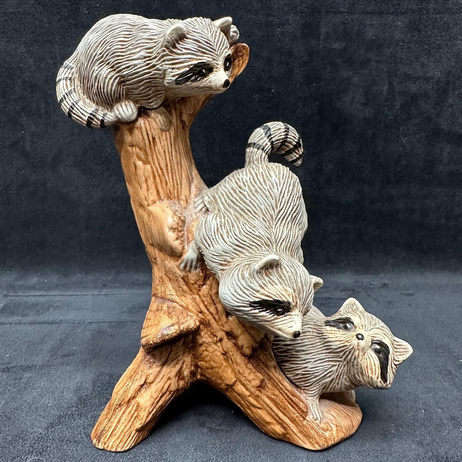 Ceramic Raccoon Family Figurine in Hollow Tree Form Sculpture: Decorative ceramic figurine depicting a family of raccoons climbing and resting on a hollow tree trunk. Finished in naturalistic brown, gray, and cream tones with textured fur and wood grain