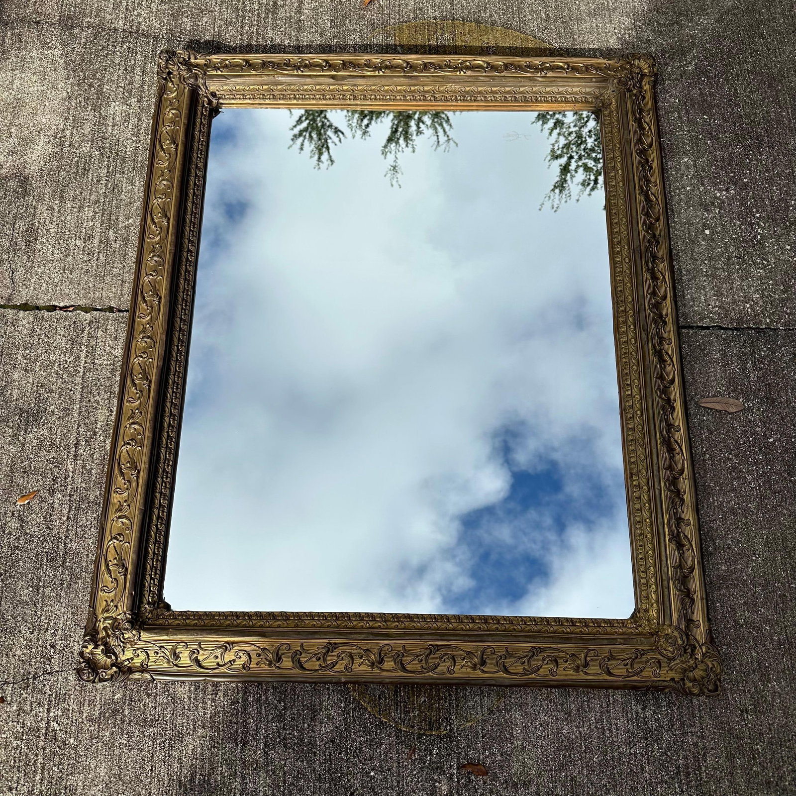 Large Antique Ornate Gilt Metal and Wood Wall Mirror Victorian Baroque Revival Style: An antique-style wall mirror featuring an ornate, gilt-metal frame decorated with scrolling leaves and floral motifs. The rectangular mirror plate is housed within a wide border of deeply molded ornam