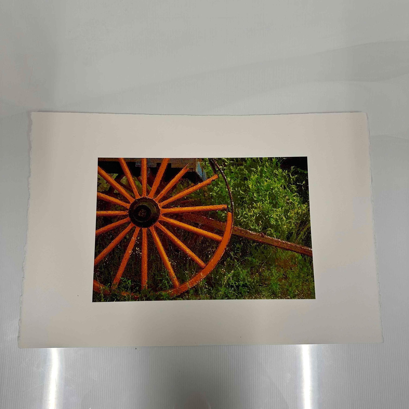 Rustic Wagon Wheel Fine Art Print on Arches France Deckle-Edge Paper: Fine art print of a rustic wagon wheel set against green foliage. Printed on high-quality Arches France watercolor paper, deckle-edged, known for its durability and artist-grade texture. Light ha