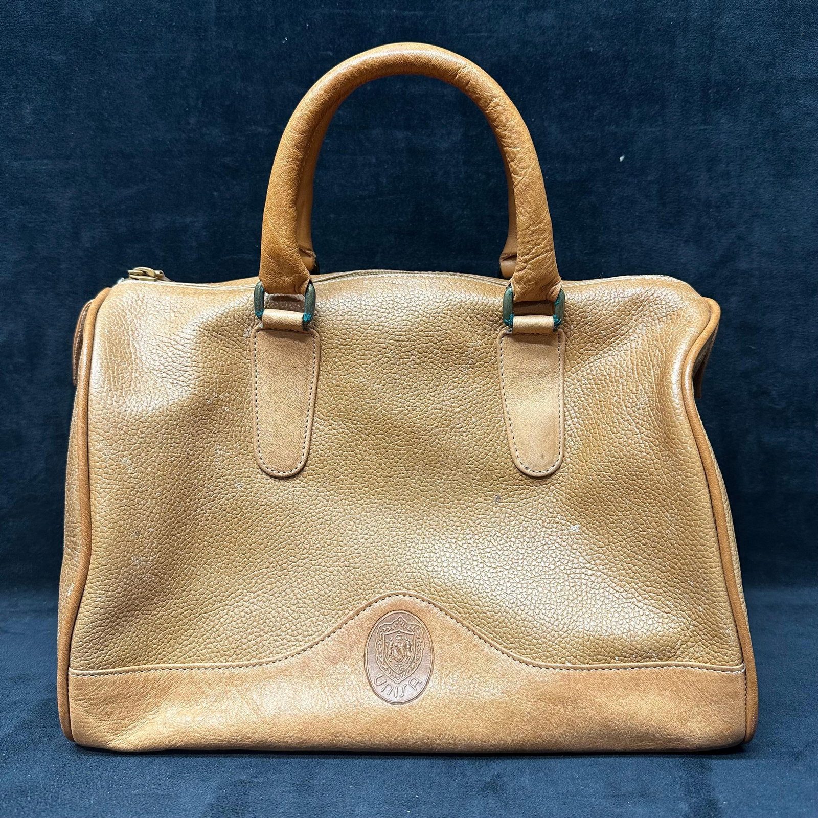 UNISA Tan Leather Satchel Handbag with Detachable Shoulder Strap: Structured UNISA leather satchel in tan pebble-grain leather. Features dual top handles, top zip closure, interior zip pocket, embossed UNISA crest logo, and a detachable leather shoulder strap.