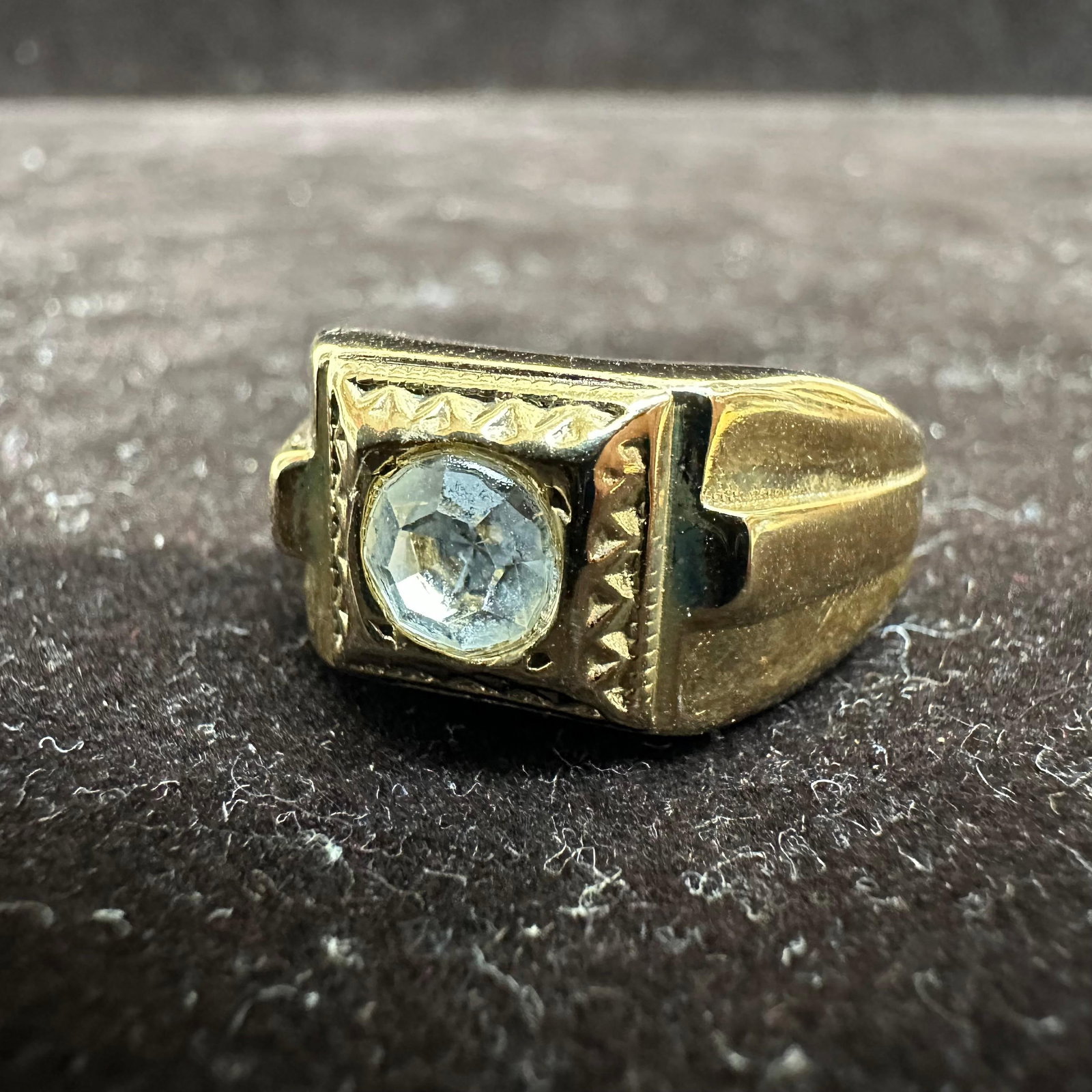 Men's Gold-Plated Ring with Clear Faceted Stone: Bold men's gold-plated ring featuring a round faceted clear stone set in a raised square bezel with detailed geometric borders. This item is in good pre-owned, previously displayed condition 