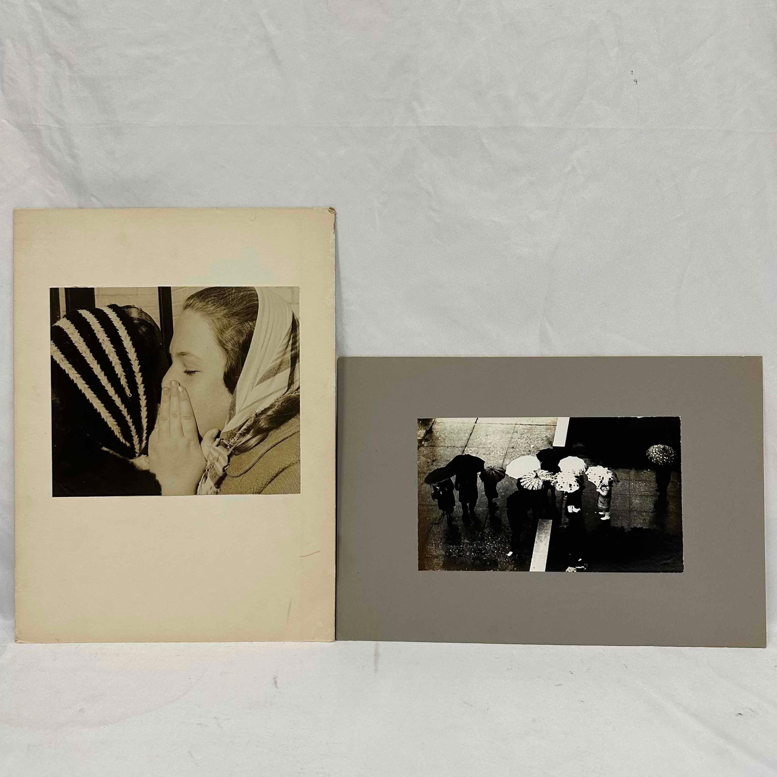 Pair of Vintage Black and White Photographs Women and Umbrellas: Lot of two striking vintage photographs, both mounted and signed by (unknown) on reverse. The first depicts a candid close-up of two women, one with a striped headscarf, in an intimate moment. The sec