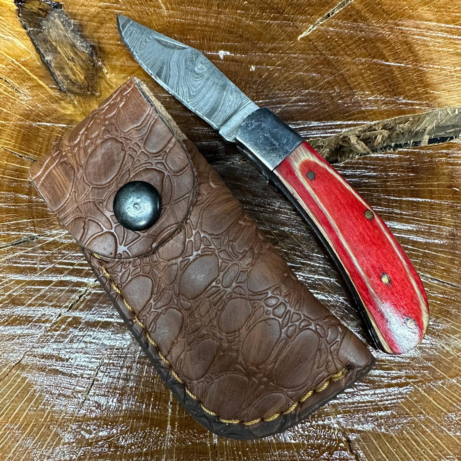 MHS Cutlery Steel Pocket Knife with Wood Handle and Leather Sheath P48: MHS Cutlery folding knife featuring a patterned steel blade and a contoured red-toned wood handle. Includes a fitted brown leather sheath. Blade locks open; folding mechanism operates smoothly. This