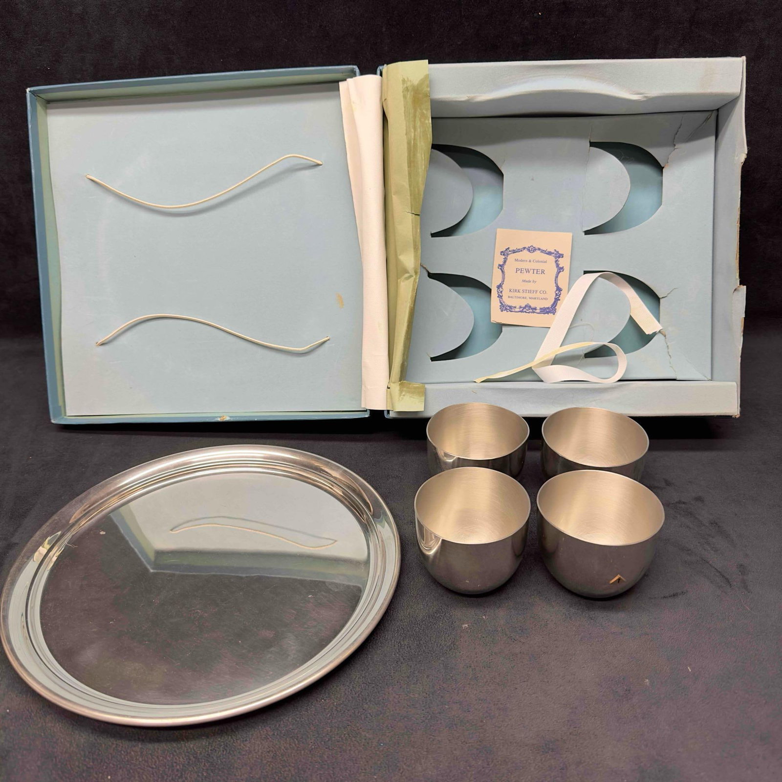 Modern and Colonial Pewter Kirk Stieff Plate and Four Jefferson Cup Set: Modern and Colonial Pewter Kirk Stieff Plate and Four Jefferson Cup Set. This set includes four Pewter cups and one plate. Includes original box that shows wear and is ripped and broken. These it