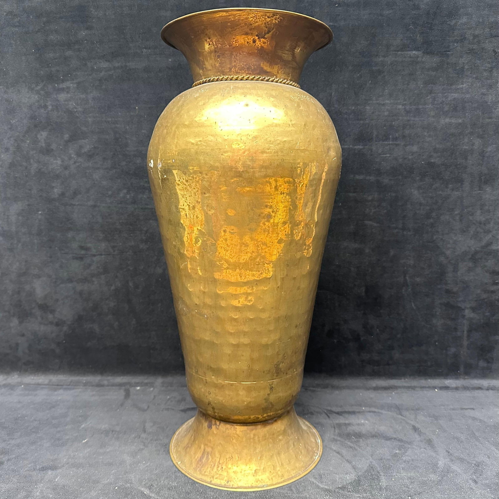Vintage Hand Hammered Brass Vase with Grape Motif Accents: Tall vintage hand-hammered brass vase featuring a flared rim, tapered body, and applied rope-style band with hanging grape cluster accents. Shows age-related patina, surface wear, and oxidation