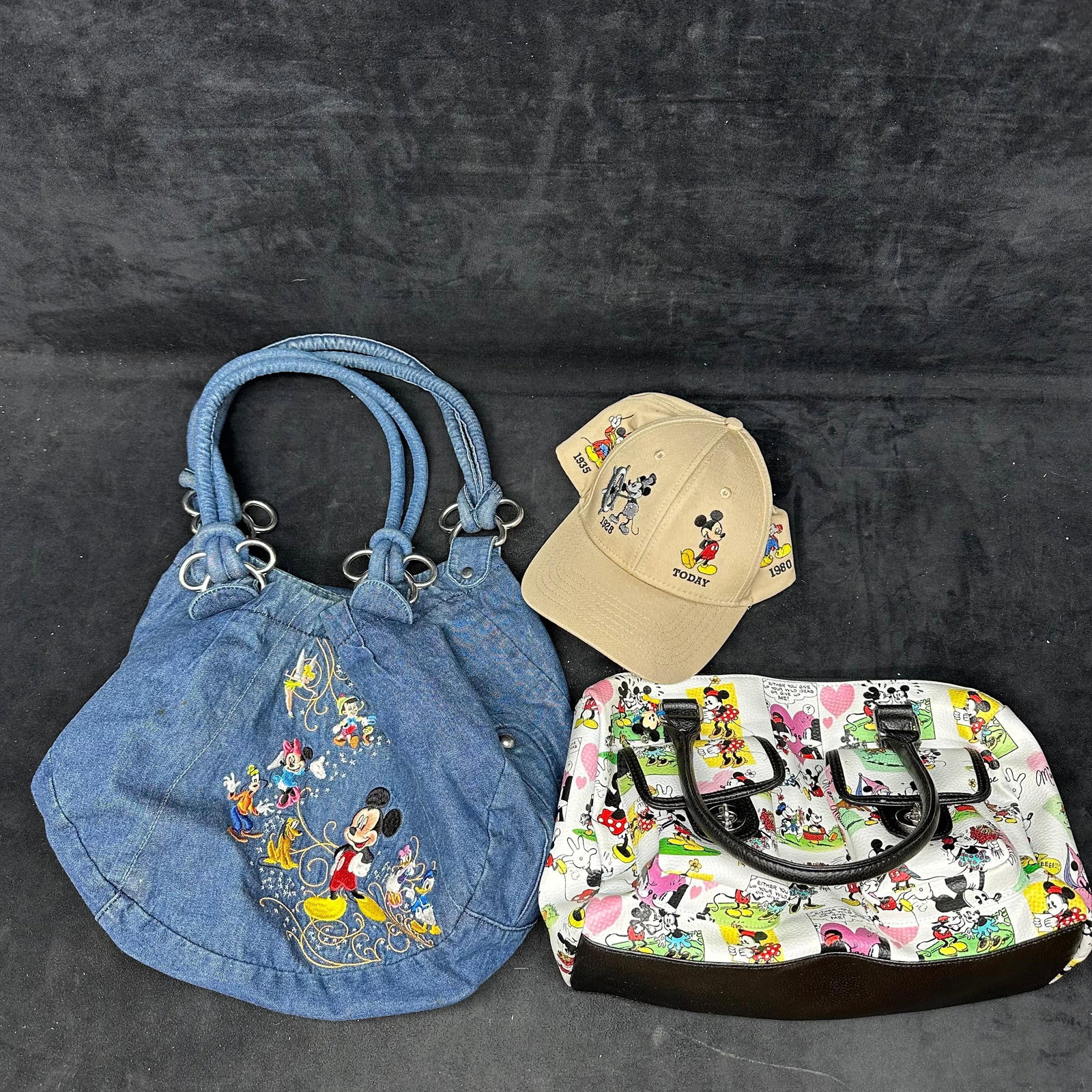 Disney Item Lot Hat and Two Handbags: Group includes one Disney denim shoulder bag with embroidered characters, one Mickey/Minnie comic-print handbag, and one Mickey Mouse evolution baseball cap, Mickey through the years, 1928-Today. All 
