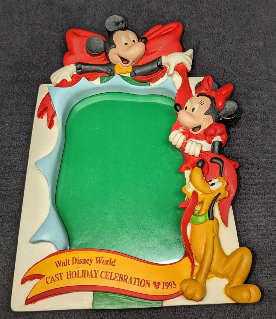 1993 Disney World Cast Exclusive Picture Frame B: 1993 Disney World Cast Exclusive Picture Frame A. Cast exclusive, Frame has Mickey Mouse, Minnie Mouse abd Pluto who are in the process of tying a big bow on the frame. Can be hung on the wall, or sit
