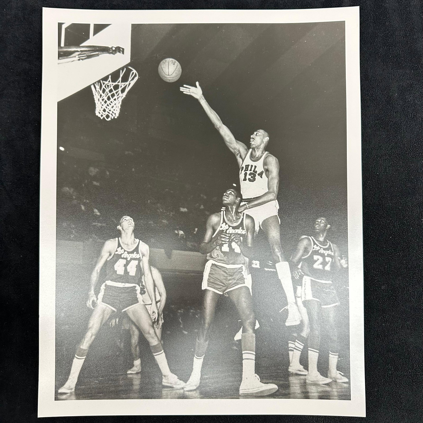 Black and White Analog Photo Print Wilt Chamberlain Record-Breaking 78 Point Game: An analog photo print capturing basketball legend Wilt Chamberlain of the Philadelphia Warriors during his historic 78-point performance. This iconic black-and-white image shows Chamberlain rising abo