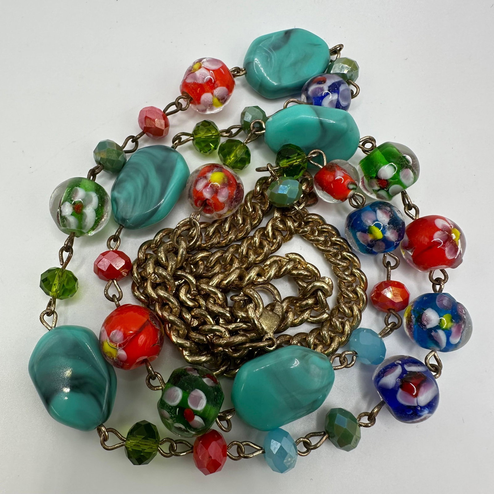 Italian Style Floral Millefiori Glass Bead Gold Tone Chain Necklace Faux Turquoise Accents: This colorful beaded necklace features a variety of vibrant glass lampwork beads, including floral millefiori patterns and faux turquoise-colored segments, connected to a gold-tone chain. This costume