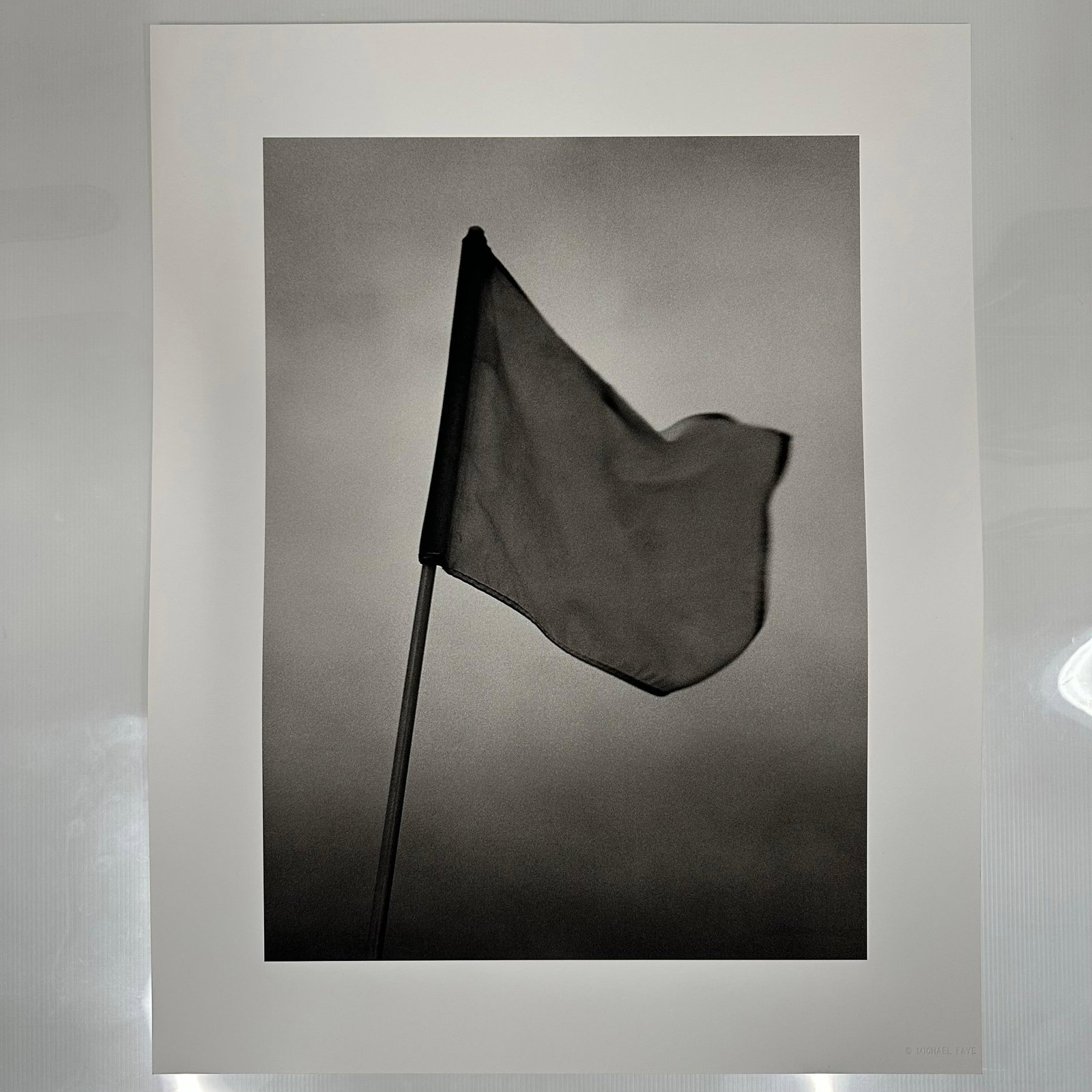 Golf Flag Michael Faye Embossed Black and White Fine Art Photograph Print: Black and white fine art photograph by Michael Faye, featuring a golf course flag gently waving in the wind against a minimalist sky. Embossed in the lower right corner, Michael Faye. Printed on