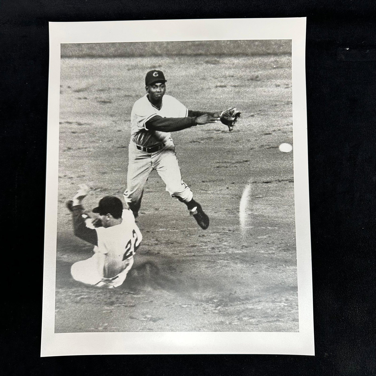 Black and White Baseball Action Analog Photo Print Infield Double Play Scene: Black and white analog photo print depicting an infield double play attempt. One player is captured mid-air, throwing the ball as a runner slides beneath. Blank reverse side. This item is in pre-owned