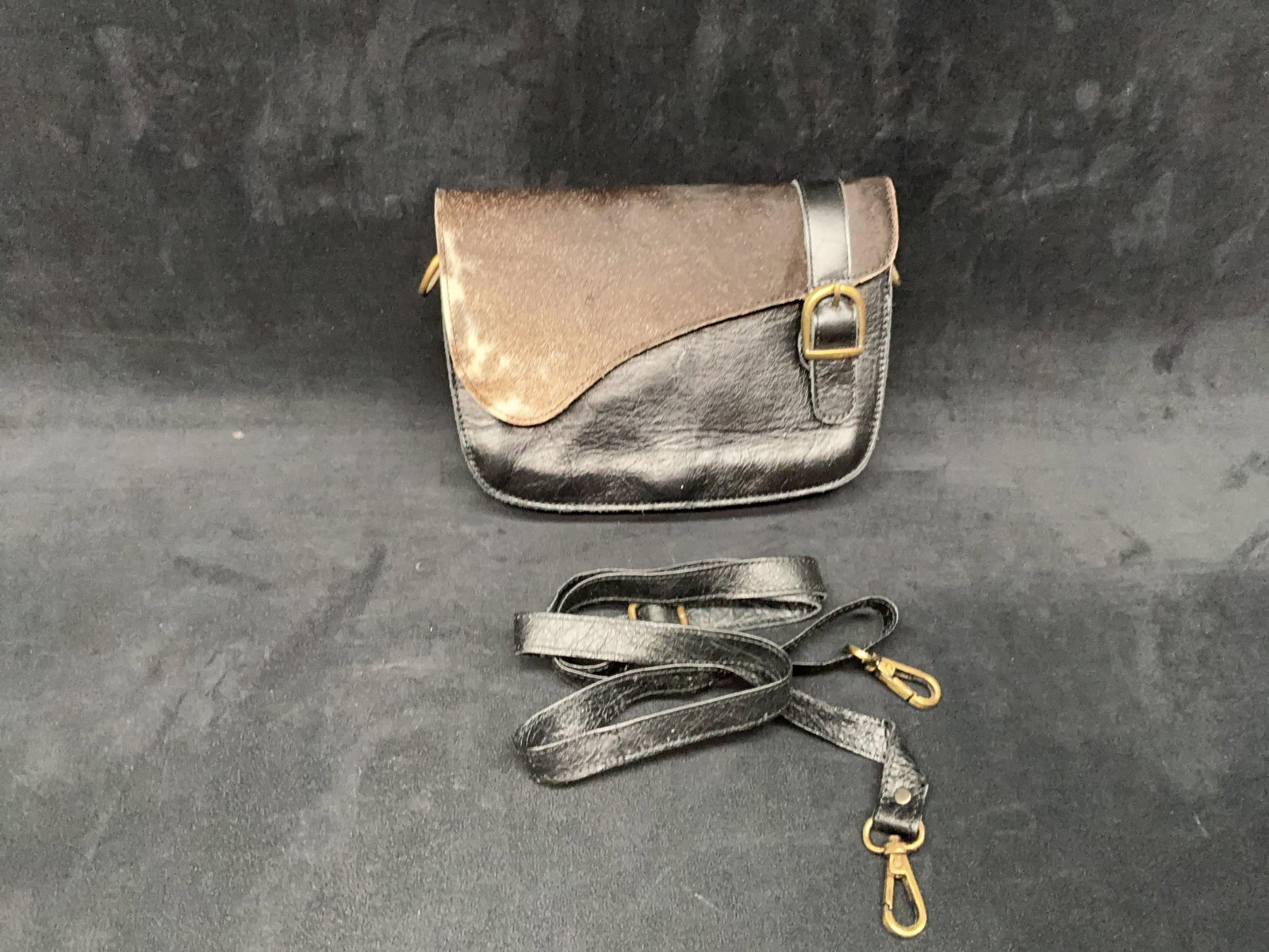 Black & Brown Cowhide Buckle Handbag: Black leather and brown hair-on cowhide handbag with flap front, buckle closure, and detachable shoulder strap. Appears unused. Please see photos for best description of condition. Approximate